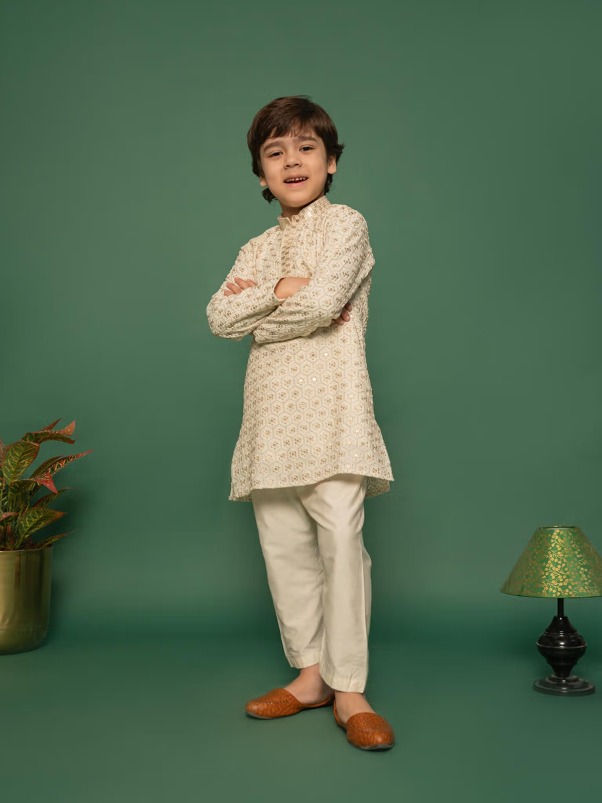 Young boy modeling boys off white kurta pyjama set Canada patterned kurta cream pyjama and brown mojari shoes on green backdrop