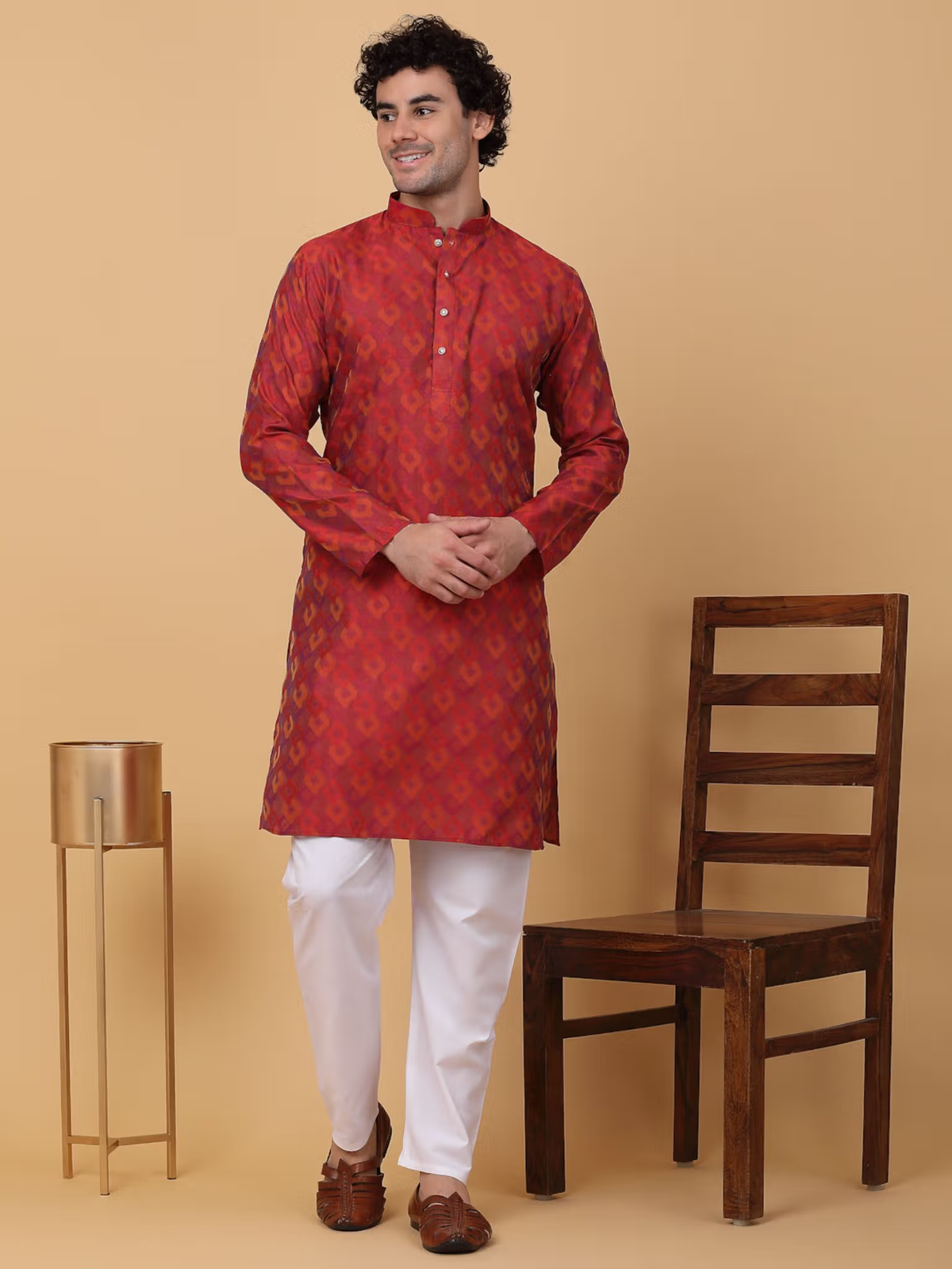 Man wearing men maroon silk kurta pajama set with white pants smiling in studio next to wooden chair