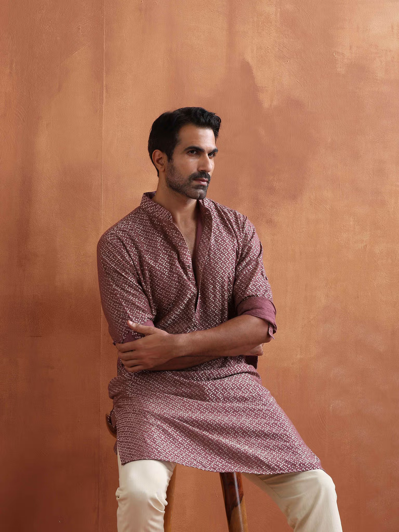 Seated model wearing men's purple cotton kurta with geometric print and rolled sleeves paired with beige trousers