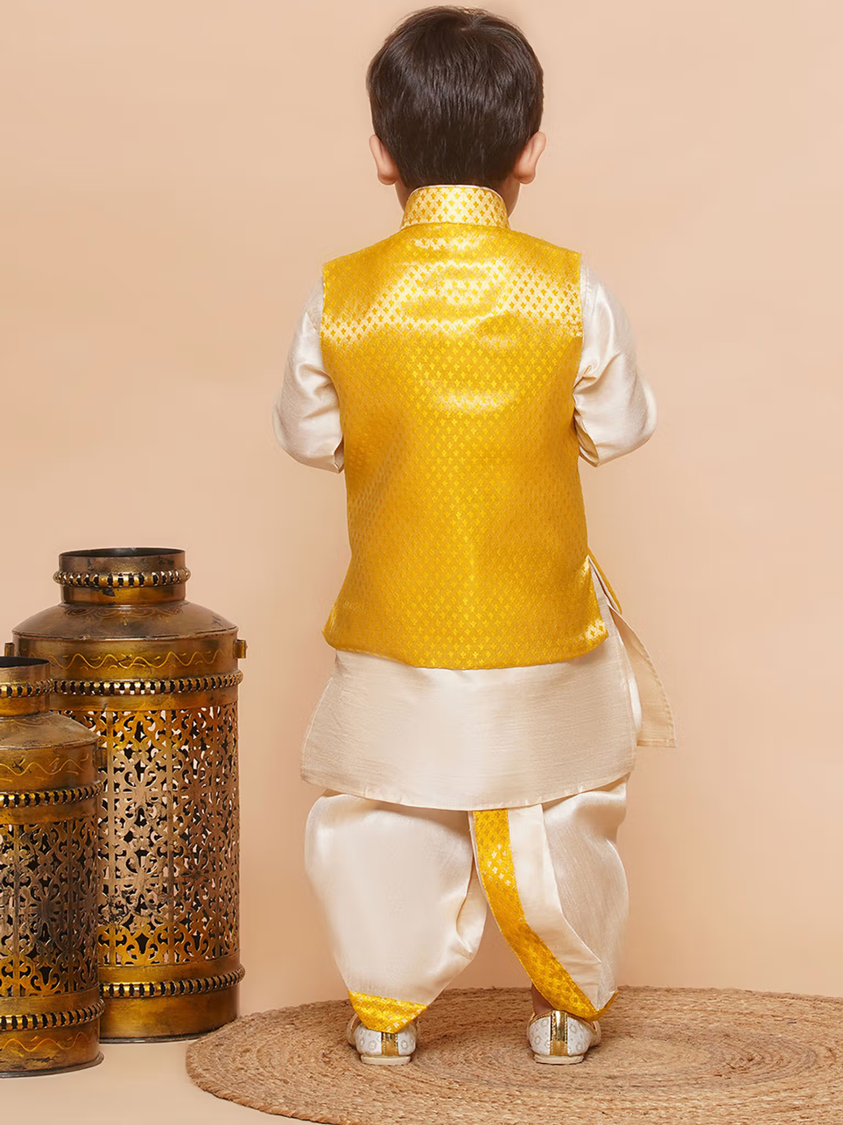 Back view of boy in boys yellow dhoti kurta set with waistcoat cream dhoti kurta and brass lanterns