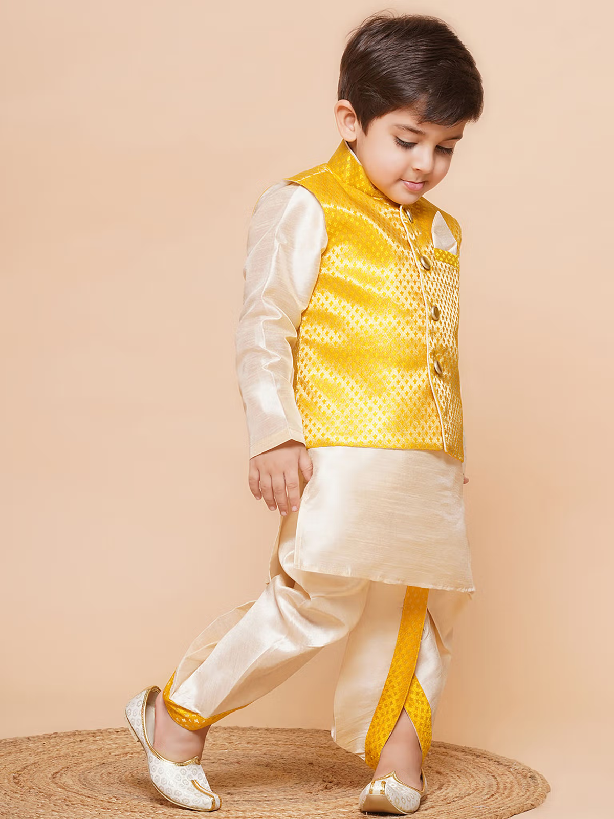 Young boy modeling boys yellow dhoti kurta set with waistcoat in cream silk kurta and traditional juttis