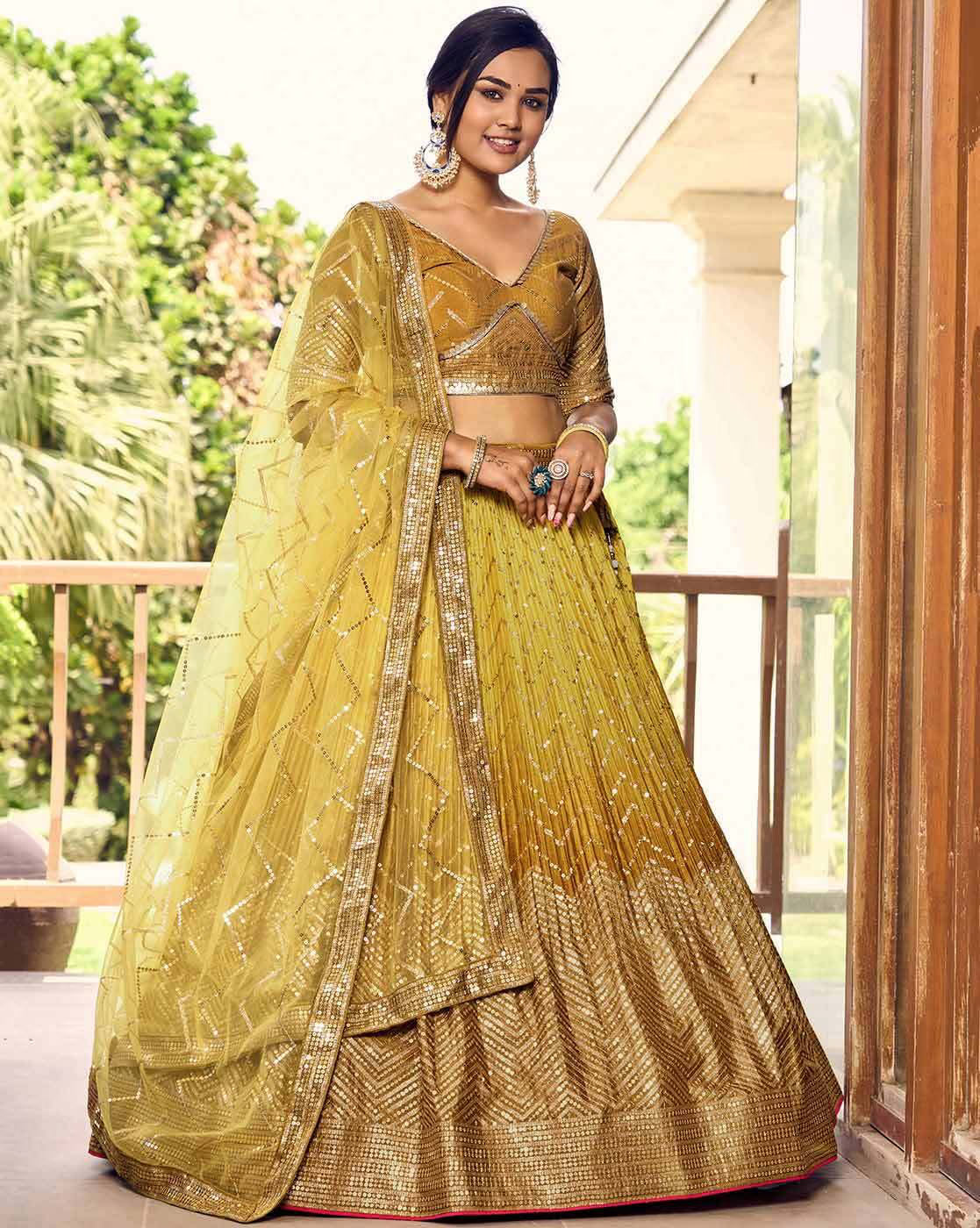 Model wearing embellished flared lehenga choli Canada in mustard gold with embroidered blouse dupatta and statement earrings