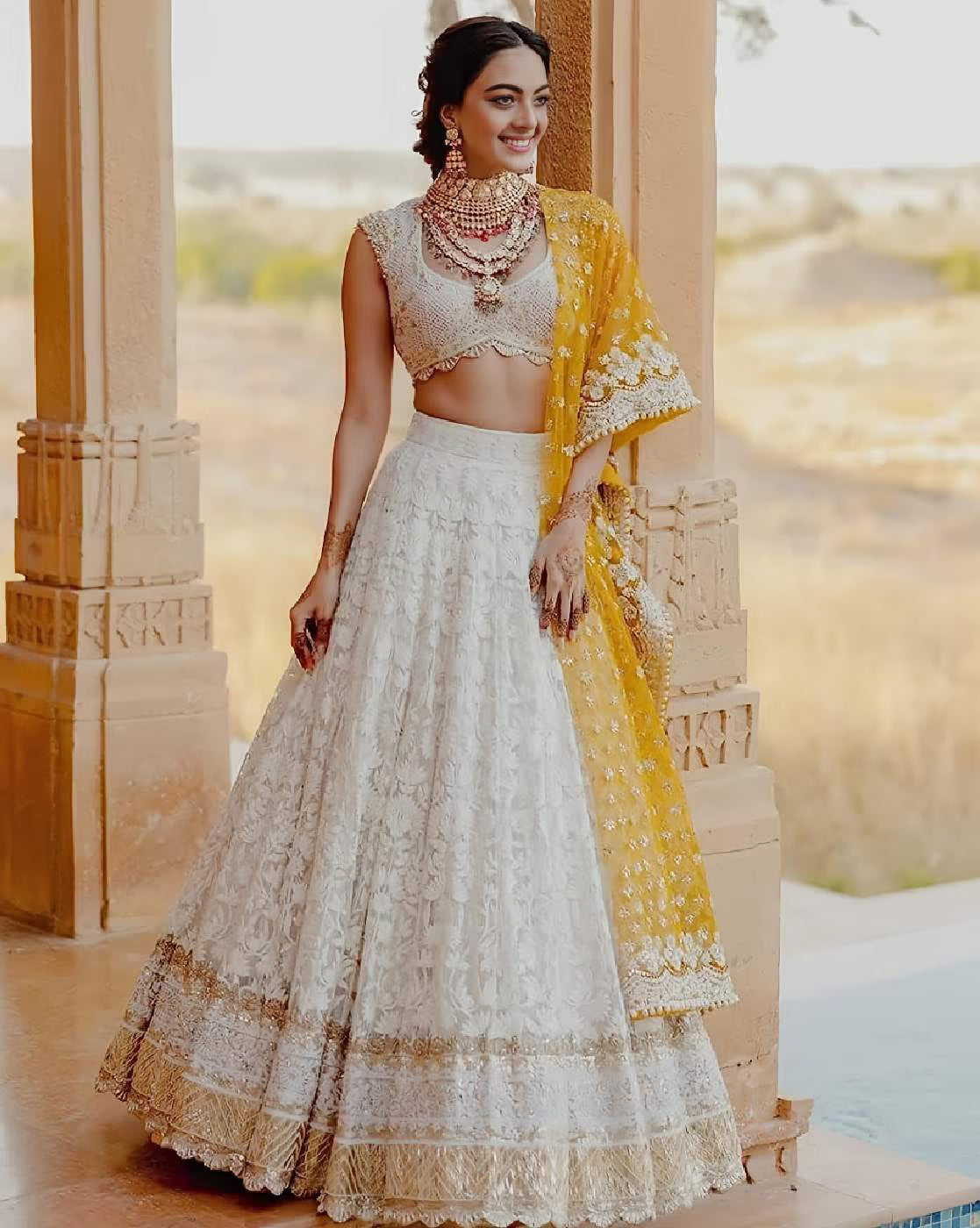 Model wearing women embellished lehenga choli set ivory lace skirt sleeveless embroidered choli and yellow dupatta
