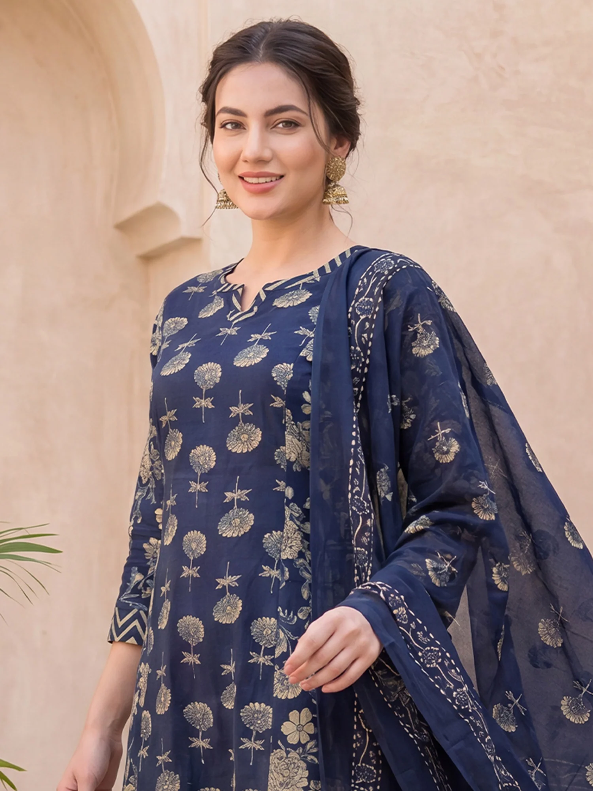 Woman wearing a navy blue traditional outfit with floral patterns against a beige wall.
