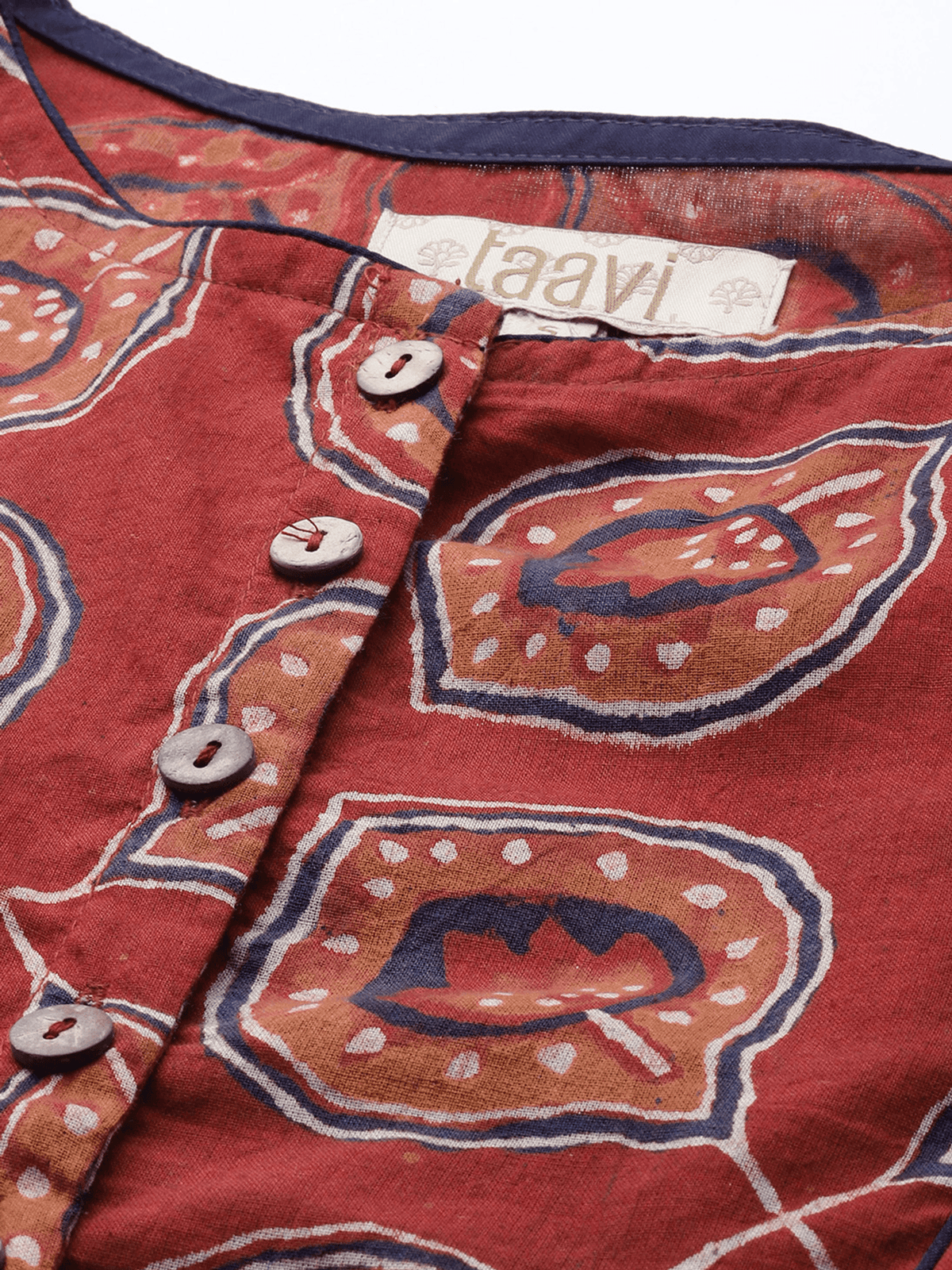 Close-up of a red patterned top with a button placket, featuring a paisley-like print in orange, navy, and white, with a visible 'raavi' neck label.