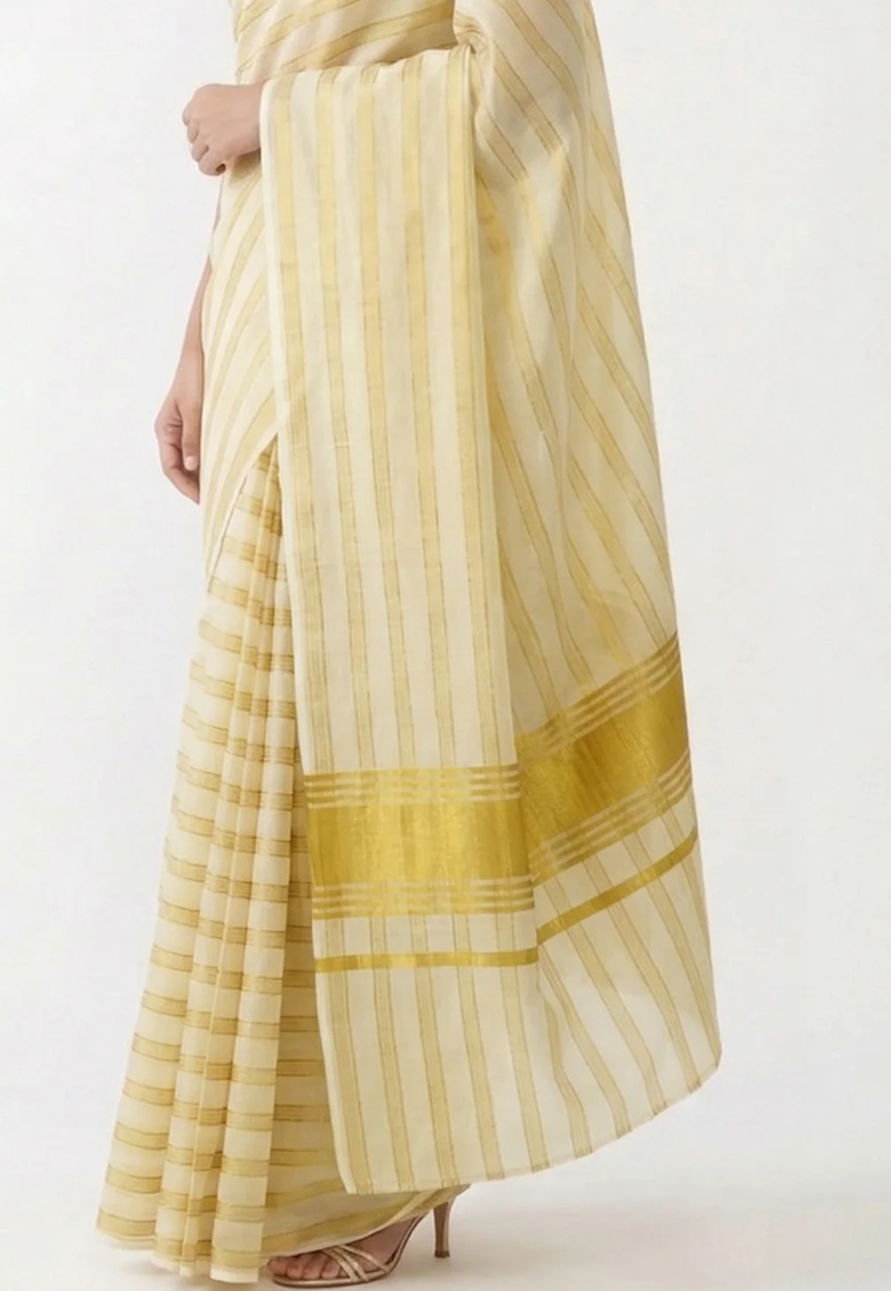 A close-up of a woman wearing a cream and yellow striped saree with a wide yellow border, shown from the waist down against a plain light background.