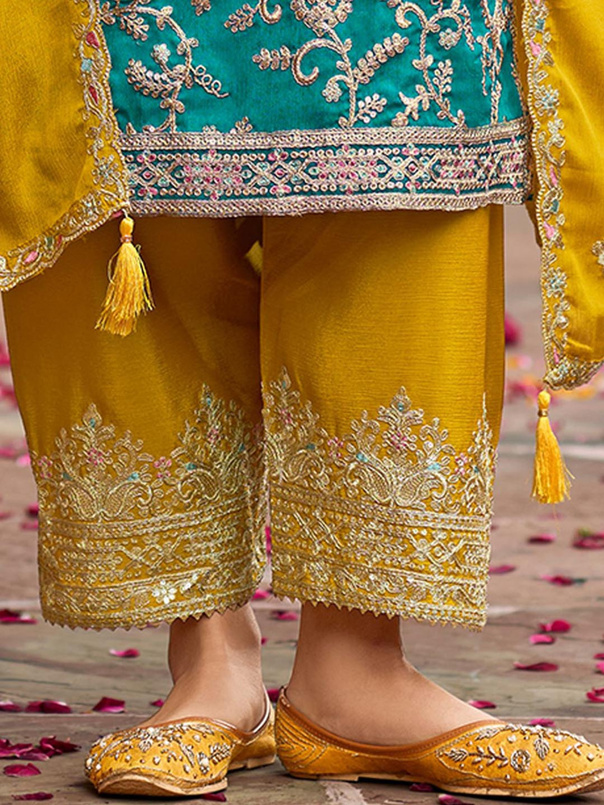 Traditional embroidered outfit with yellow pants and turquoise top on a wooden floor.