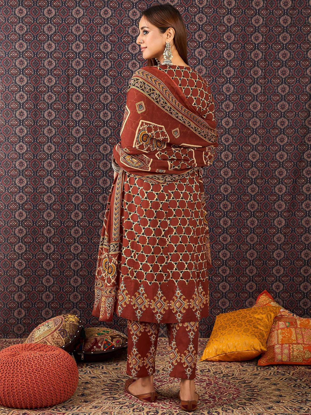 Woman wearing a patterned outfit against a decorative wall with cushions.