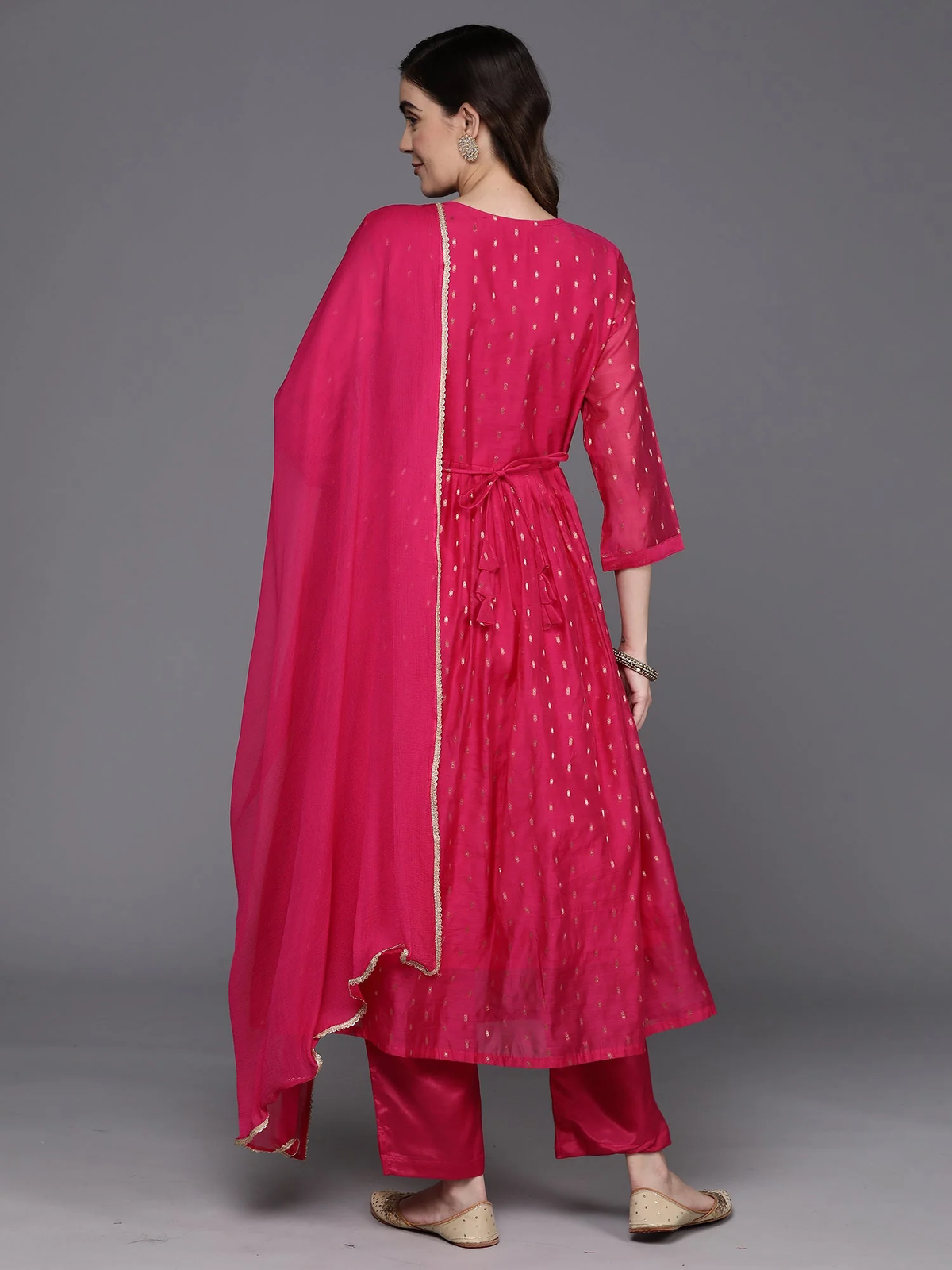 A woman modeling a bright pink traditional outfit with a matching dupatta, shown from the back against a plain gray studio background.