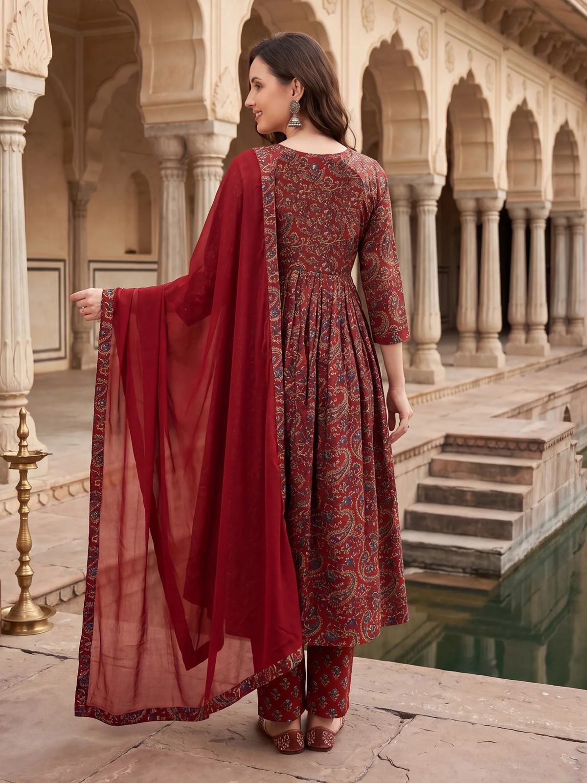 Woman in a traditional outfit standing in an architectural setting with columns and water feature.