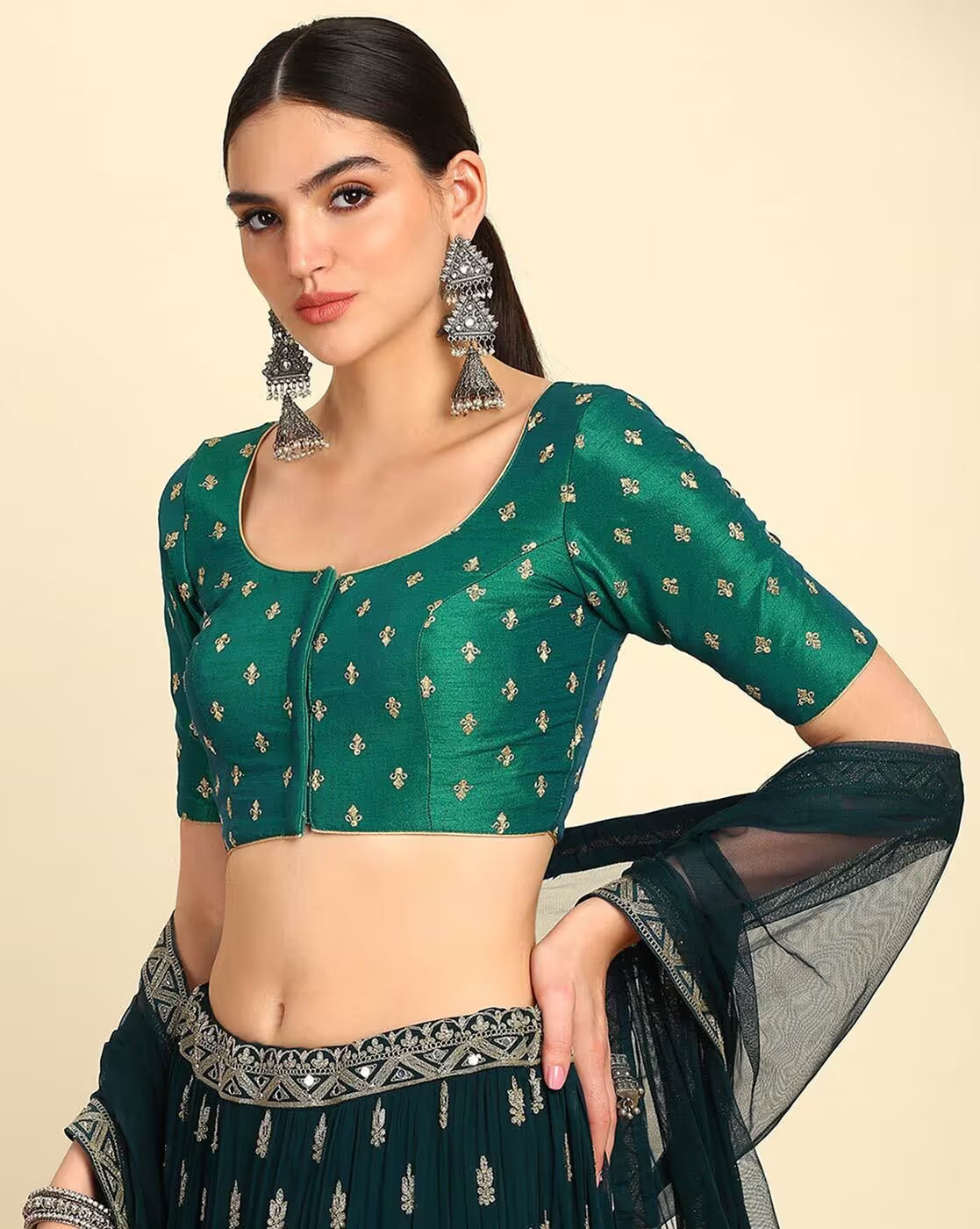 Woman wearing a green blouse with gold patterns and a matching saree on a beige background