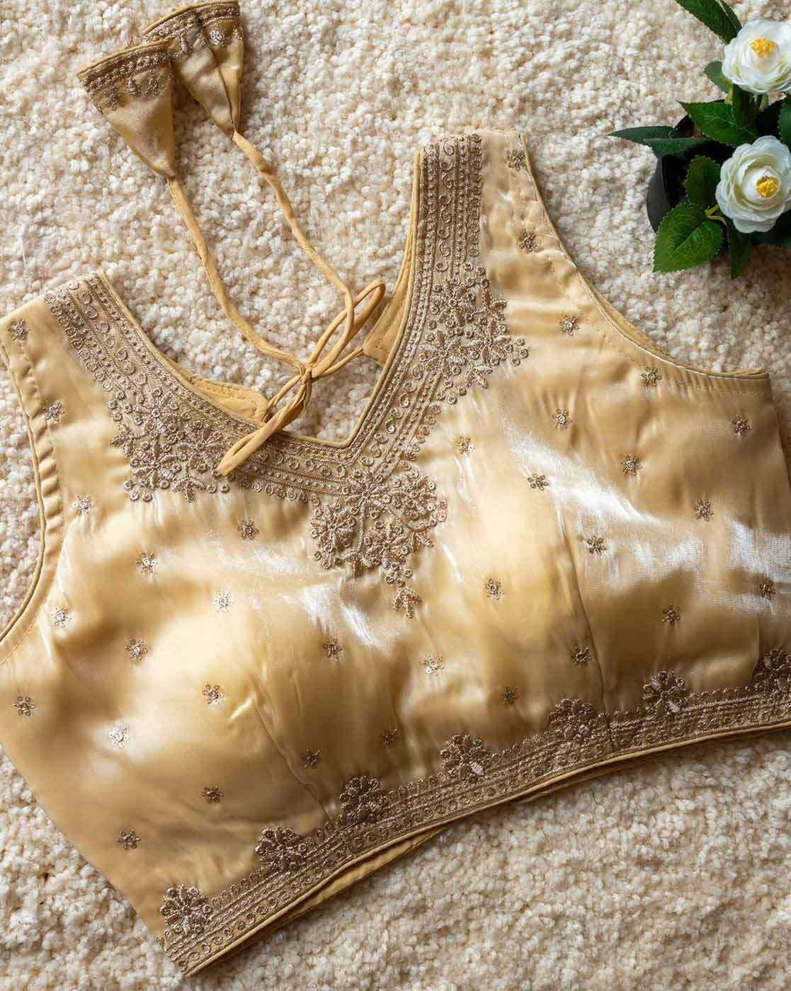 Gold embroidered blouse on a textured surface with flowers in the background