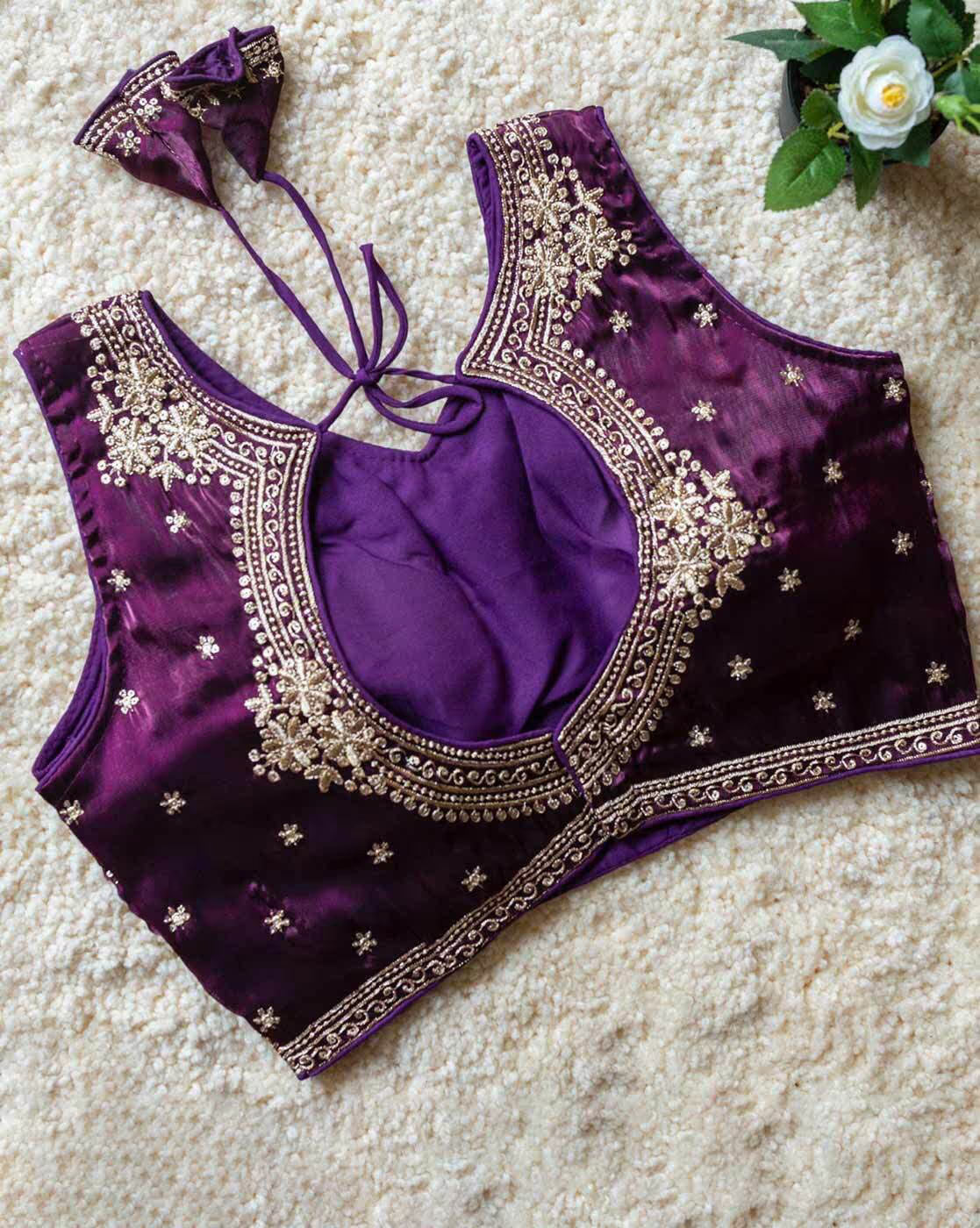 Purple blouse with intricate gold embroidery on a textured surface.