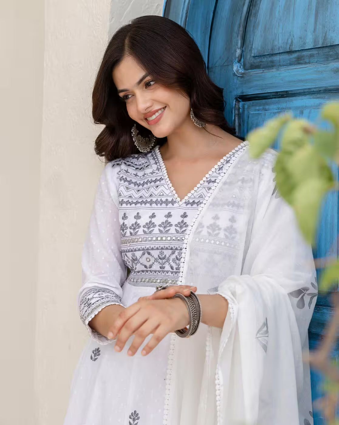 Aromie white embroidered kurta set for women with silver earrings and matching dupatta near blue door