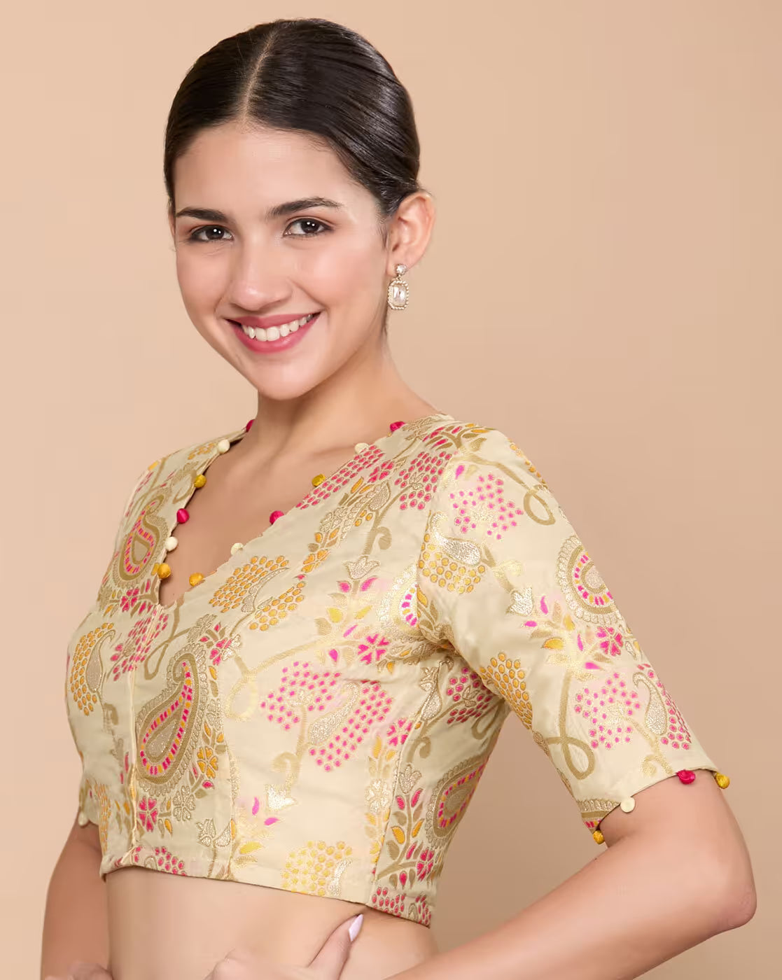 A woman modeling a beige printed blouse with pink and yellow paisley and floral motifs, set against a solid beige background.