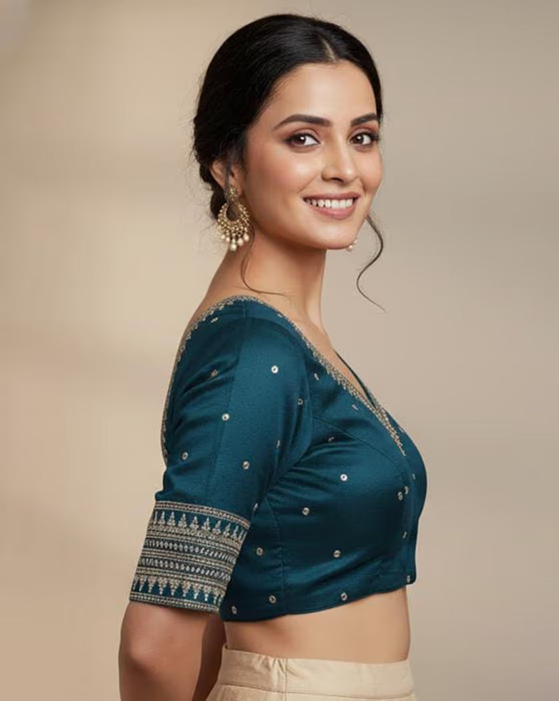 Woman wearing a teal blouse with intricate patterns on a beige background
