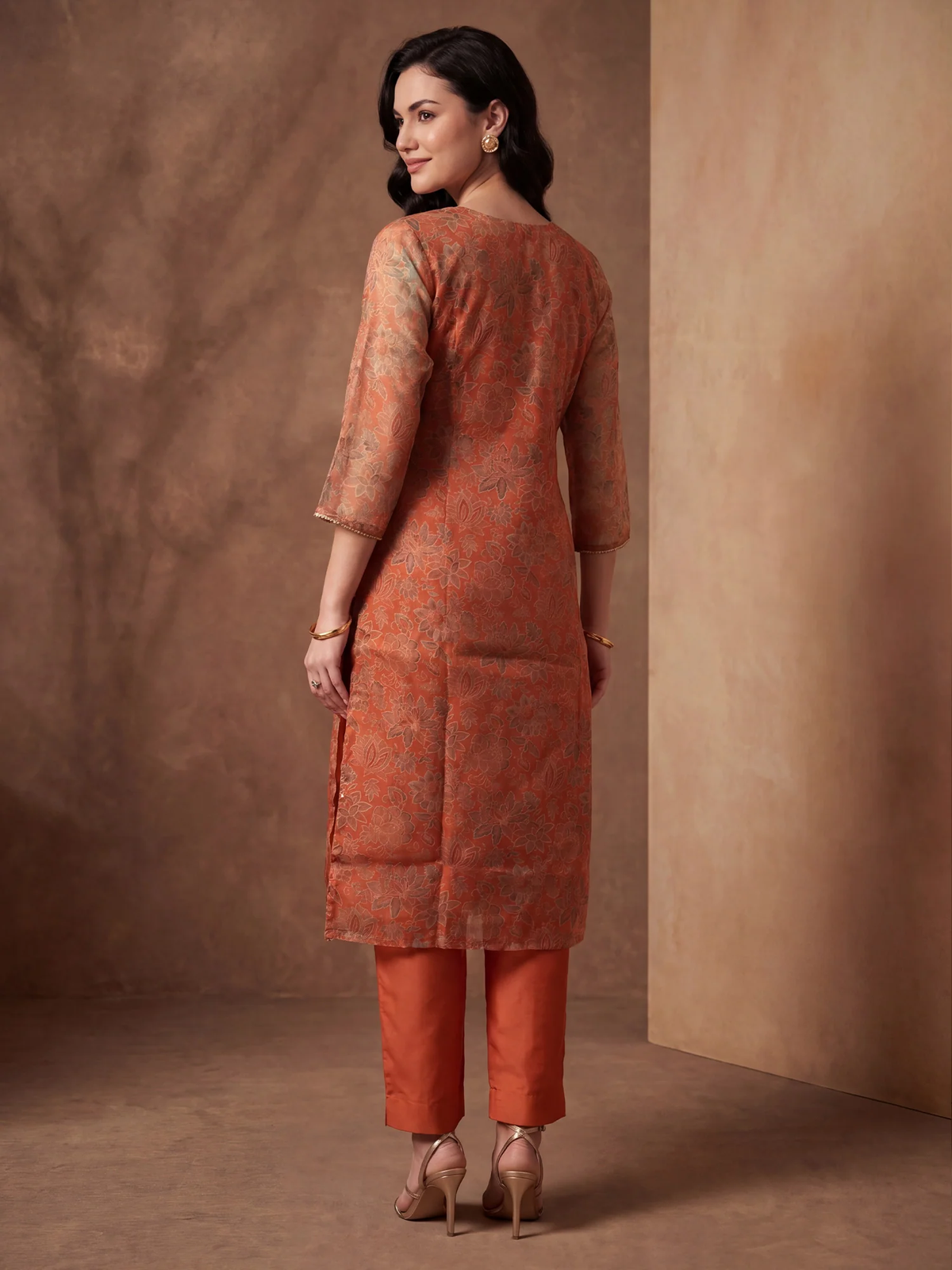Woman wearing an orange kurta with a matching pants set against a brown background