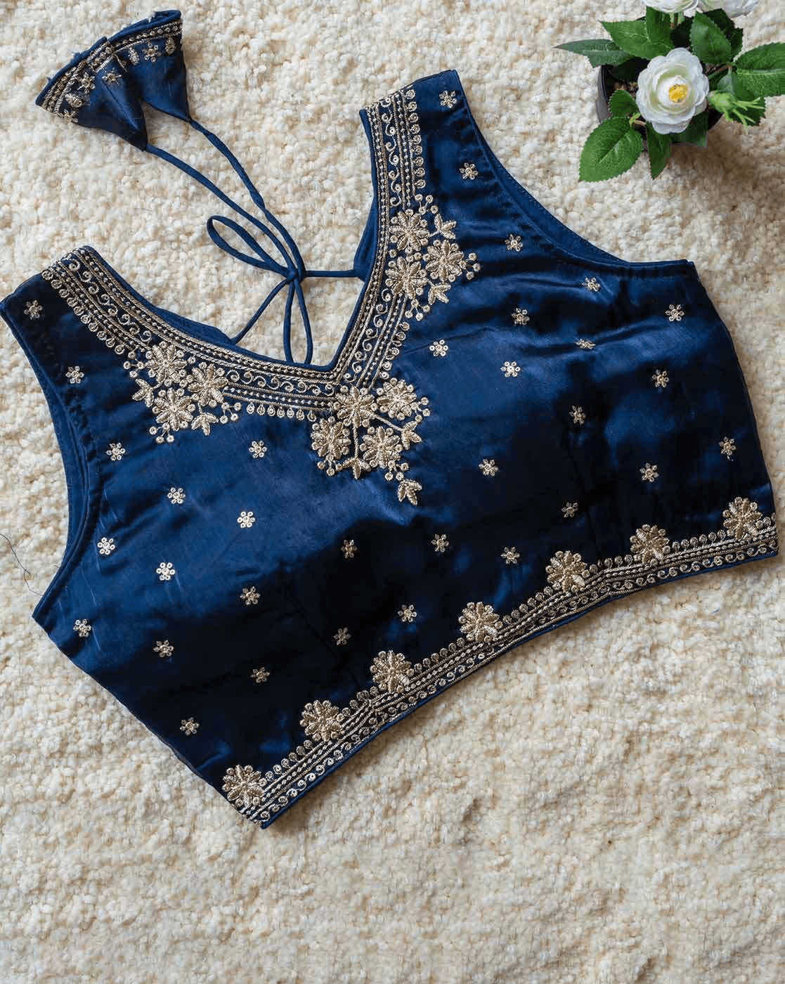 Blue embroidered top on a textured surface with a small plant in the corner