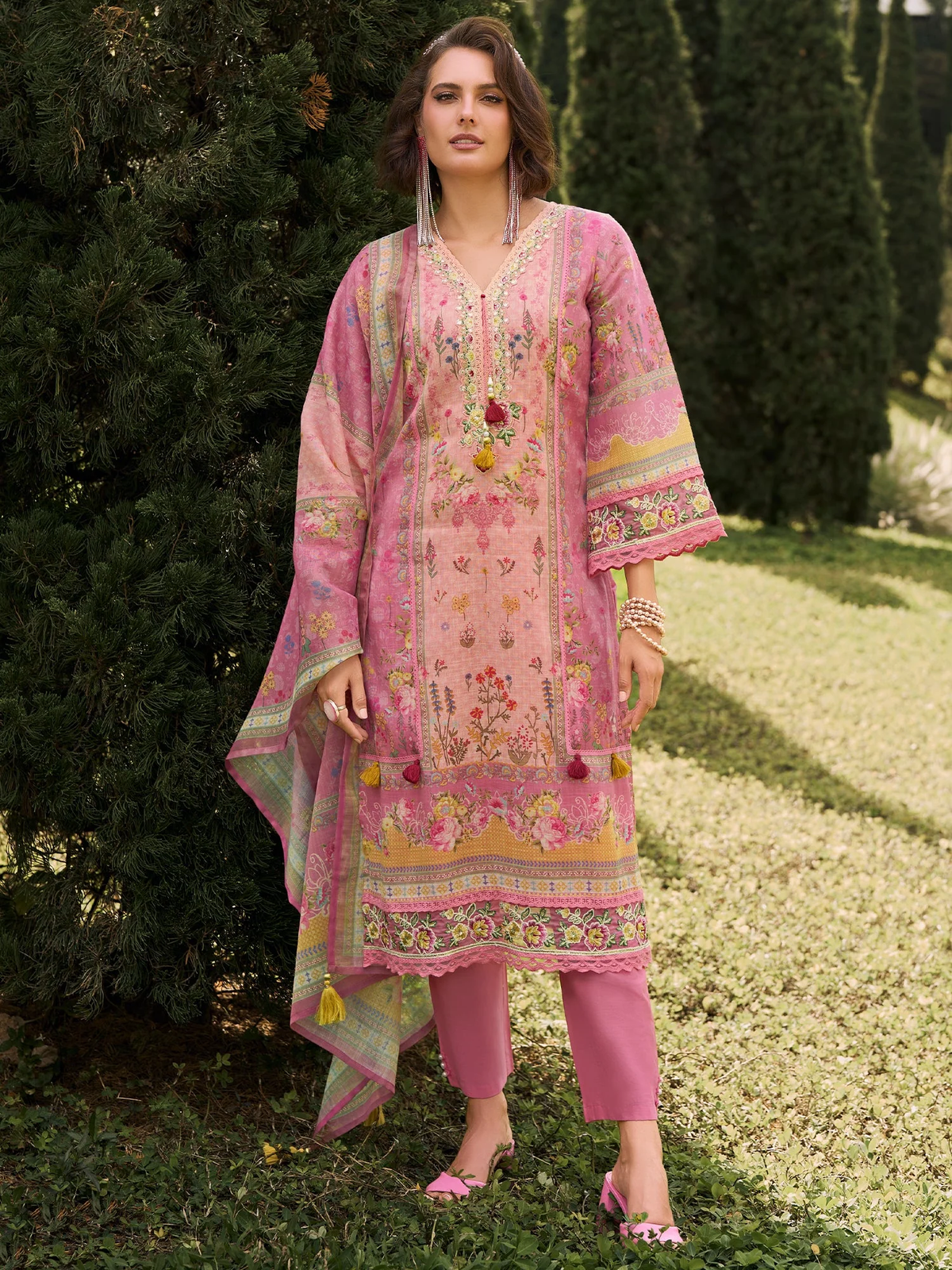 Woman wearing a pink embroidered outfit standing outdoors with greenery in the background