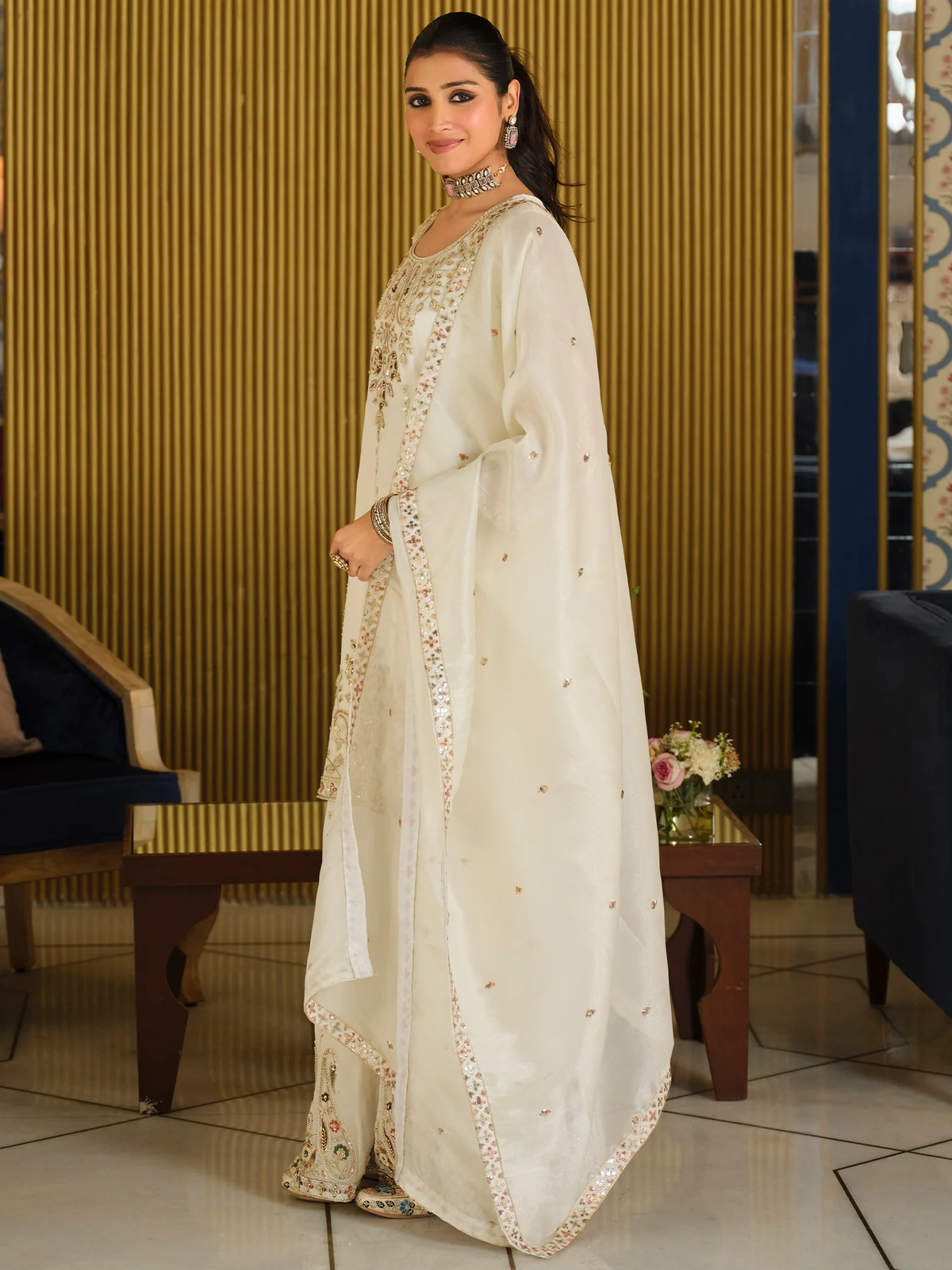 Woman in a white embroidered traditional outfit standing in an indoor setting.