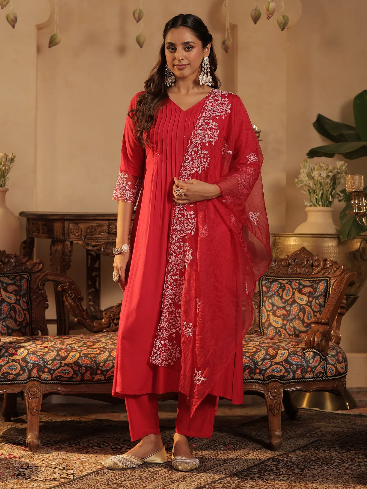 Woman in a red traditional outfit standing in an ornate room.
