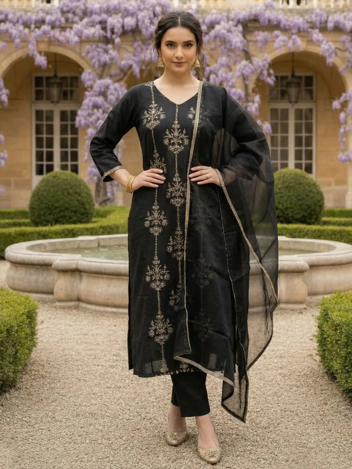 Woman in black embroidered outfit standing in a garden with floral decorations