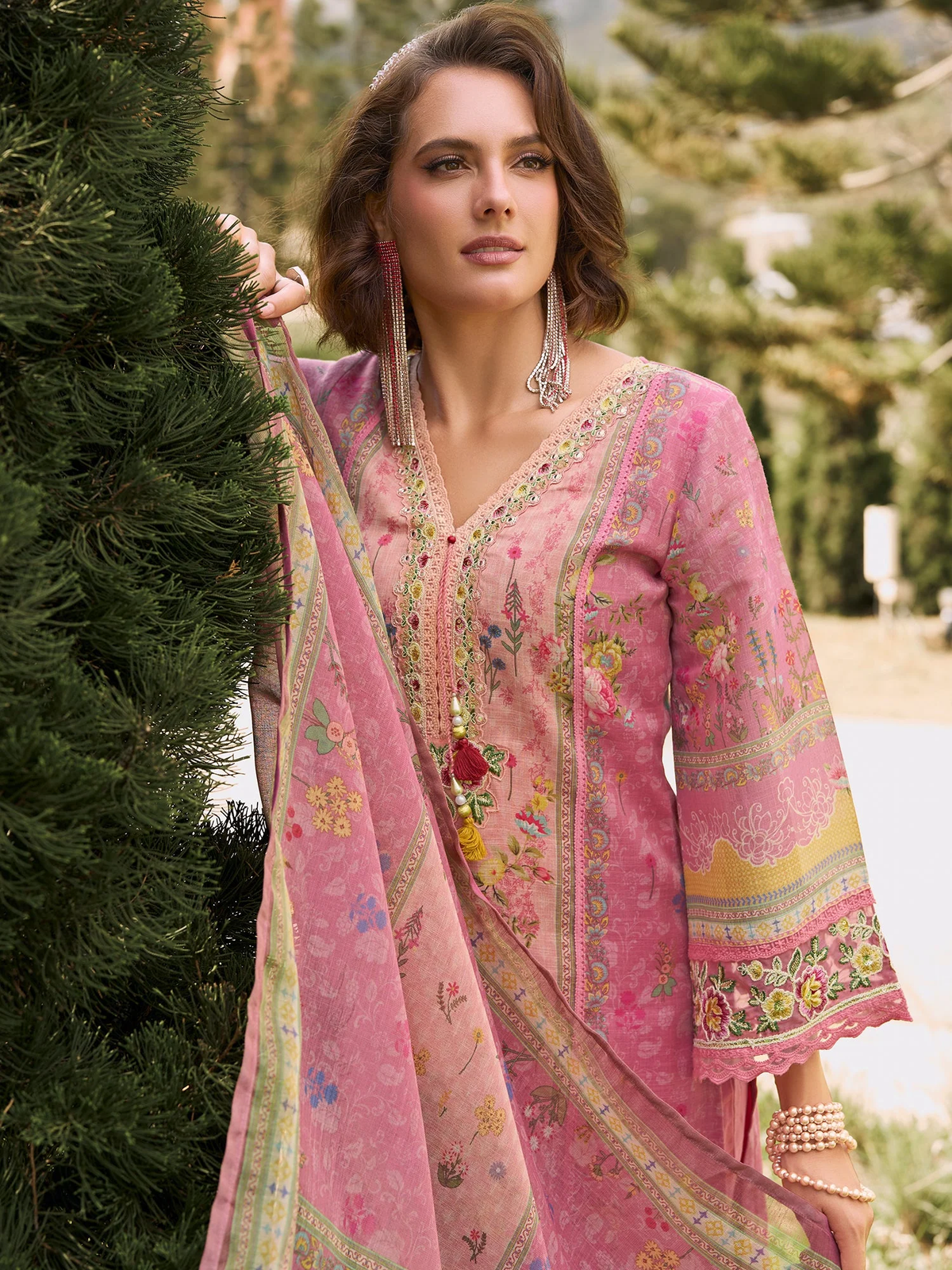 Woman wearing a pink embroidered traditional outfit with a green outdoor background