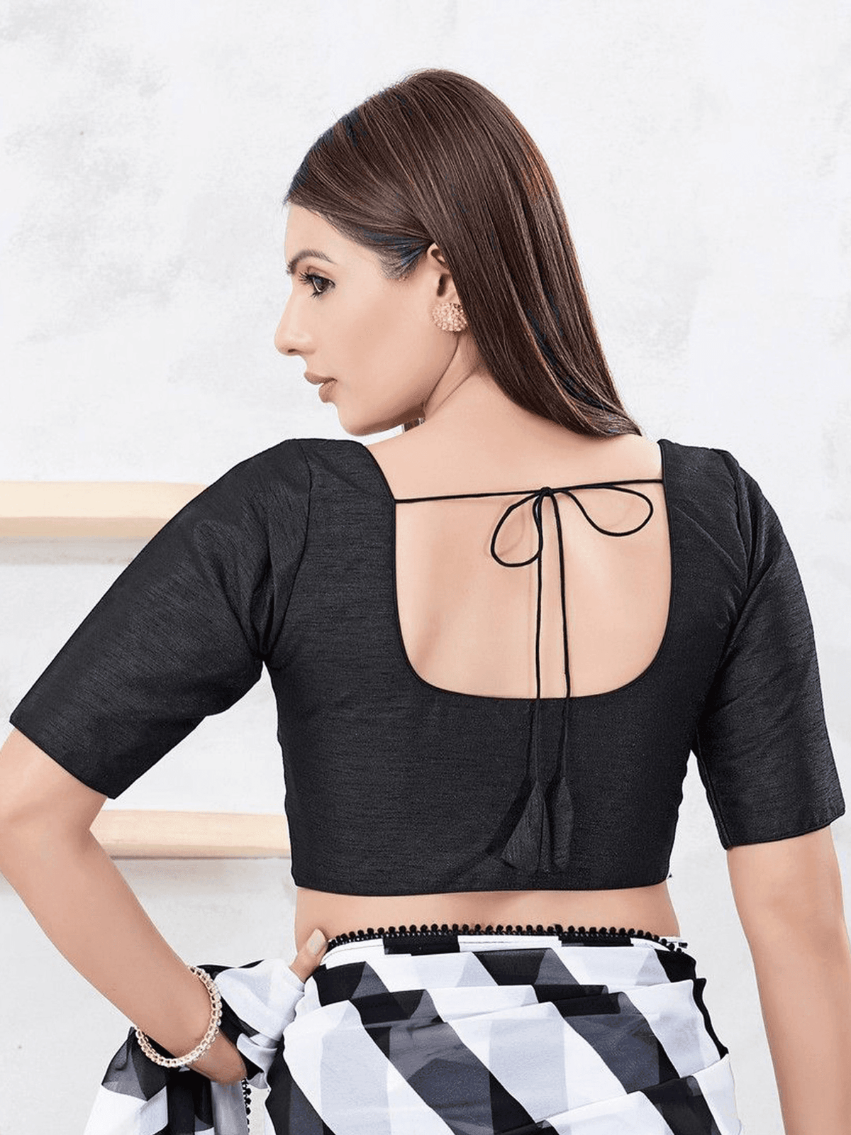 A woman shown from the back wearing a black short-sleeve blouse with a square neckline and tie-back detail, paired with a black, white, and gray patterned skirt.