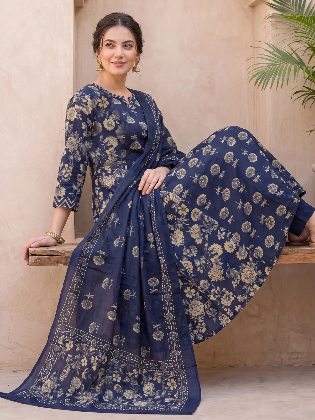 Woman wearing a blue floral saree sitting on a wooden bench.