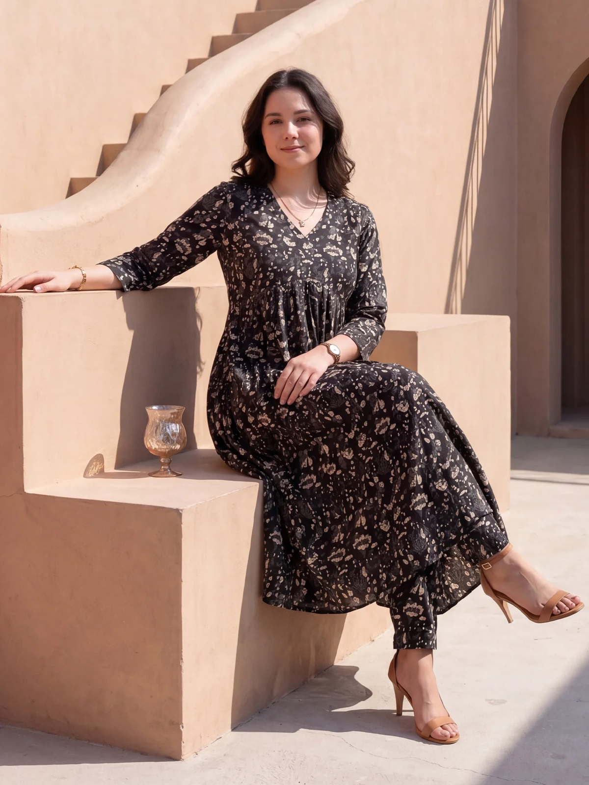 Woman in a black floral dress sitting on a beige step outdoors.