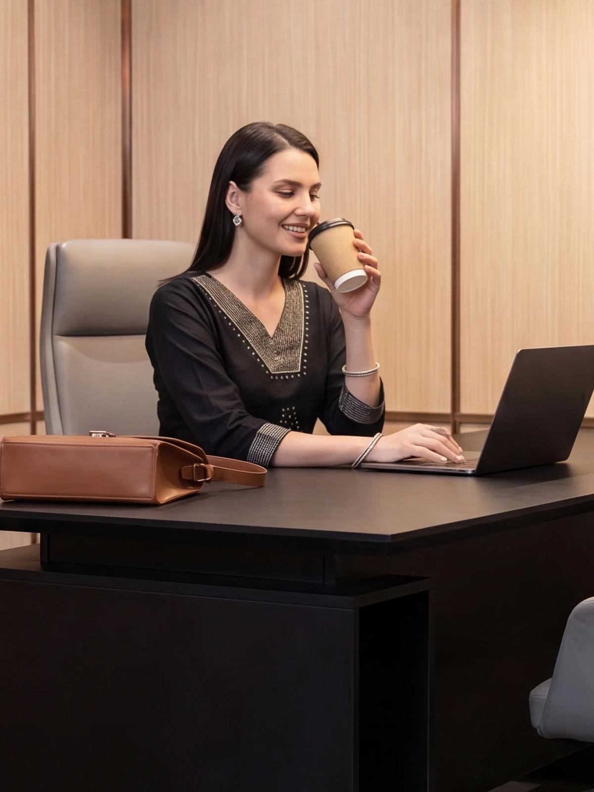 Woman sitting at a desk with a laptop and holding a coffee cup, smiling.