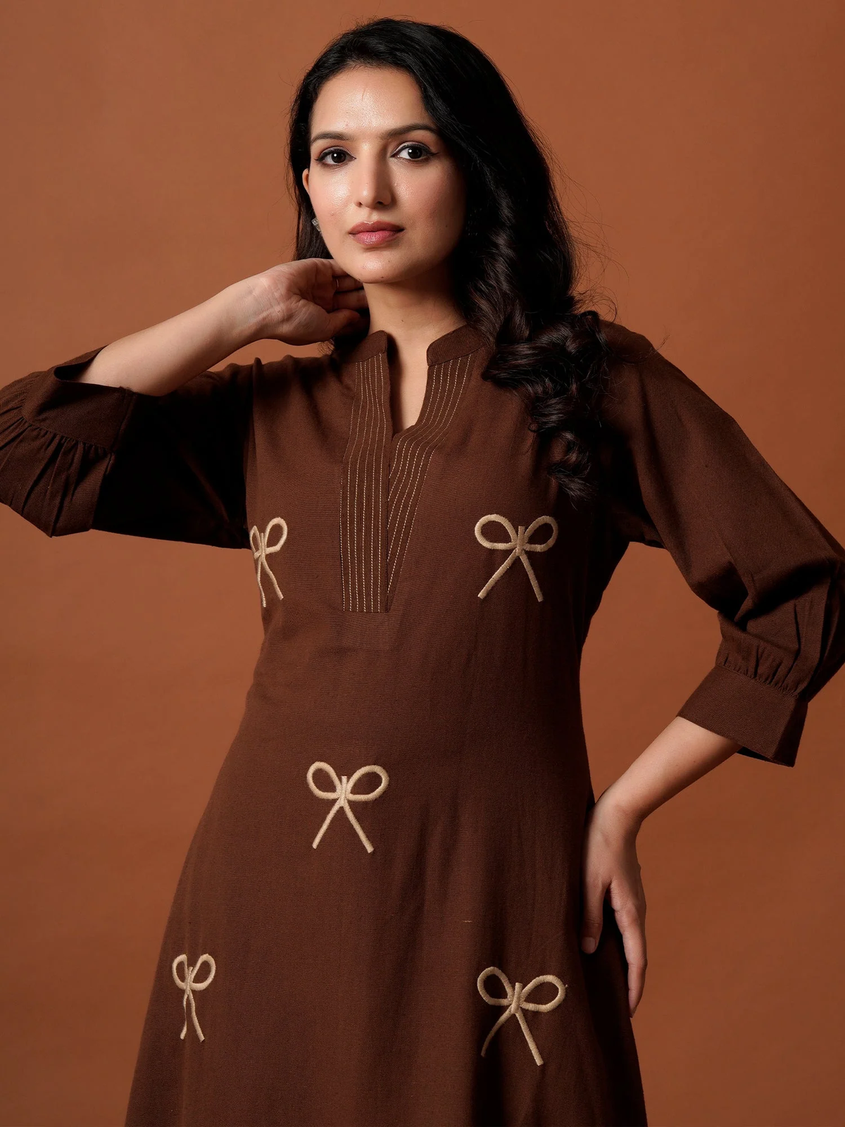 Woman wearing a brown dress with bow details against a brown background