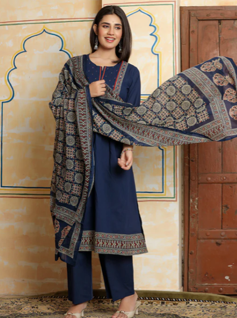A woman models a navy blue three-piece salwar kameez suit with matching printed dupatta. The kurta and trousers are solid navy blue, while the dupatta features intricate beige and gold geometric patterns.