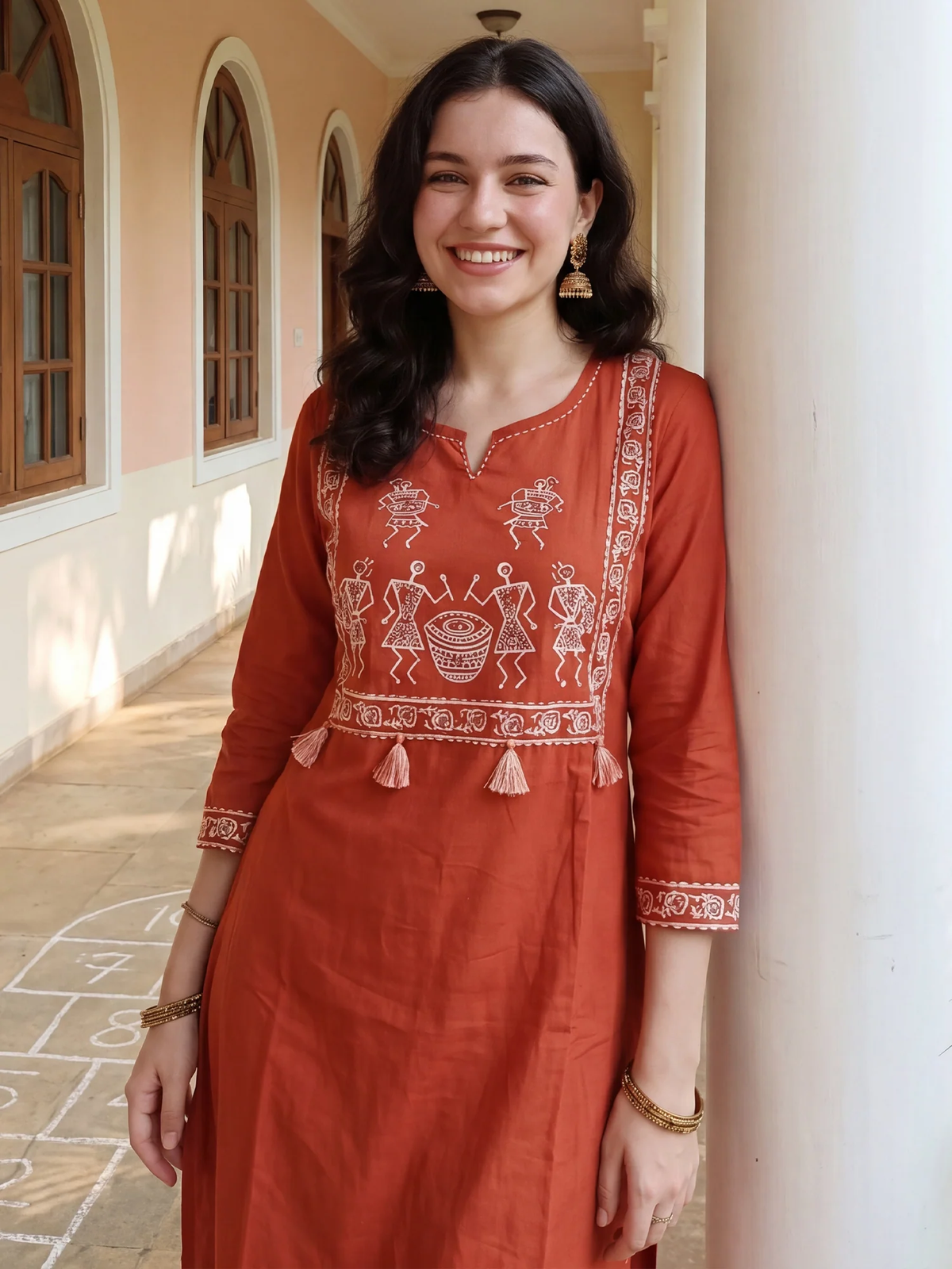 Woman wearing a traditional red embroidered outfit standing in a sunlit hallway.