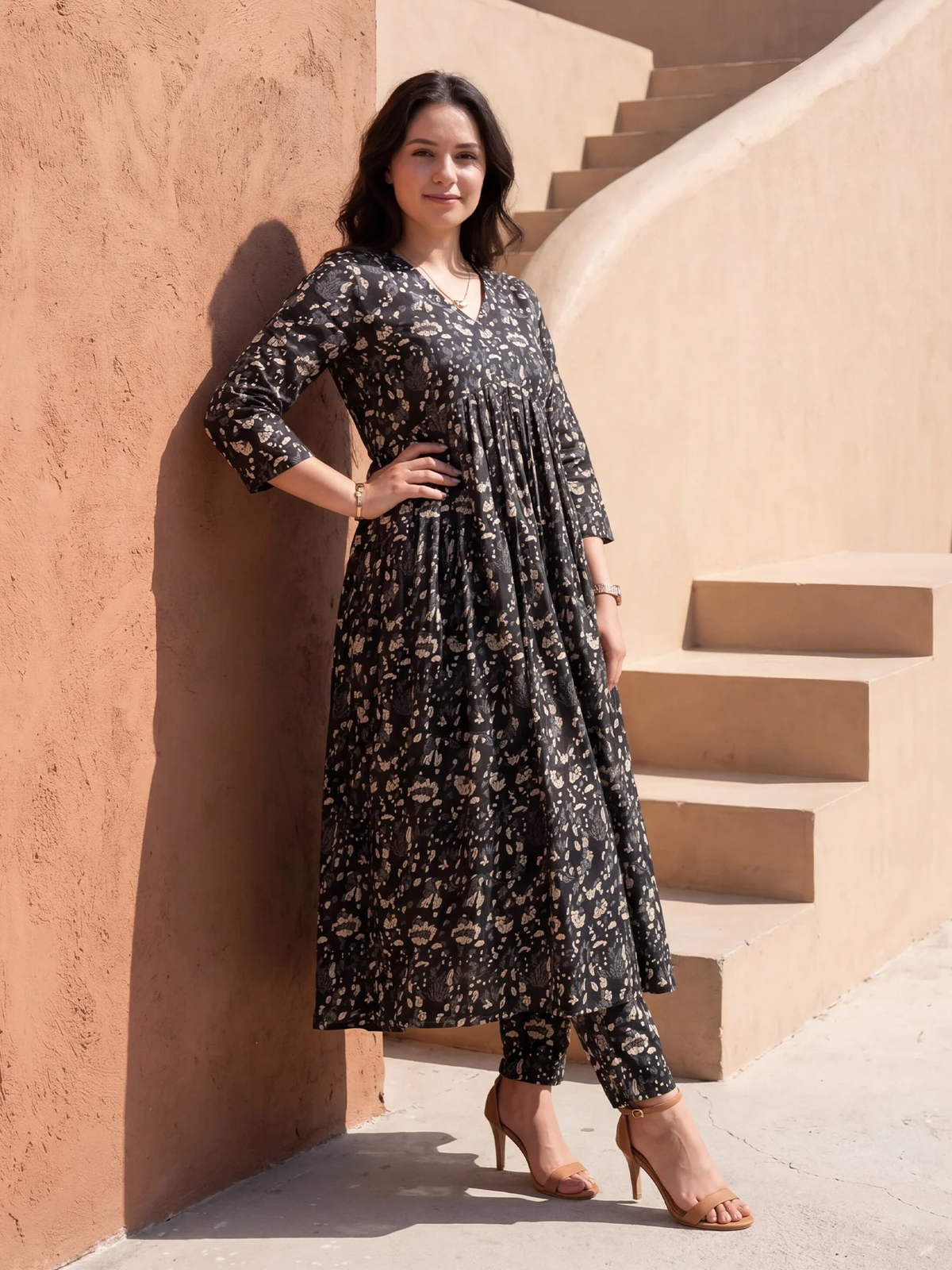 Woman in a black floral dress standing on a staircase with a warm-toned wall.