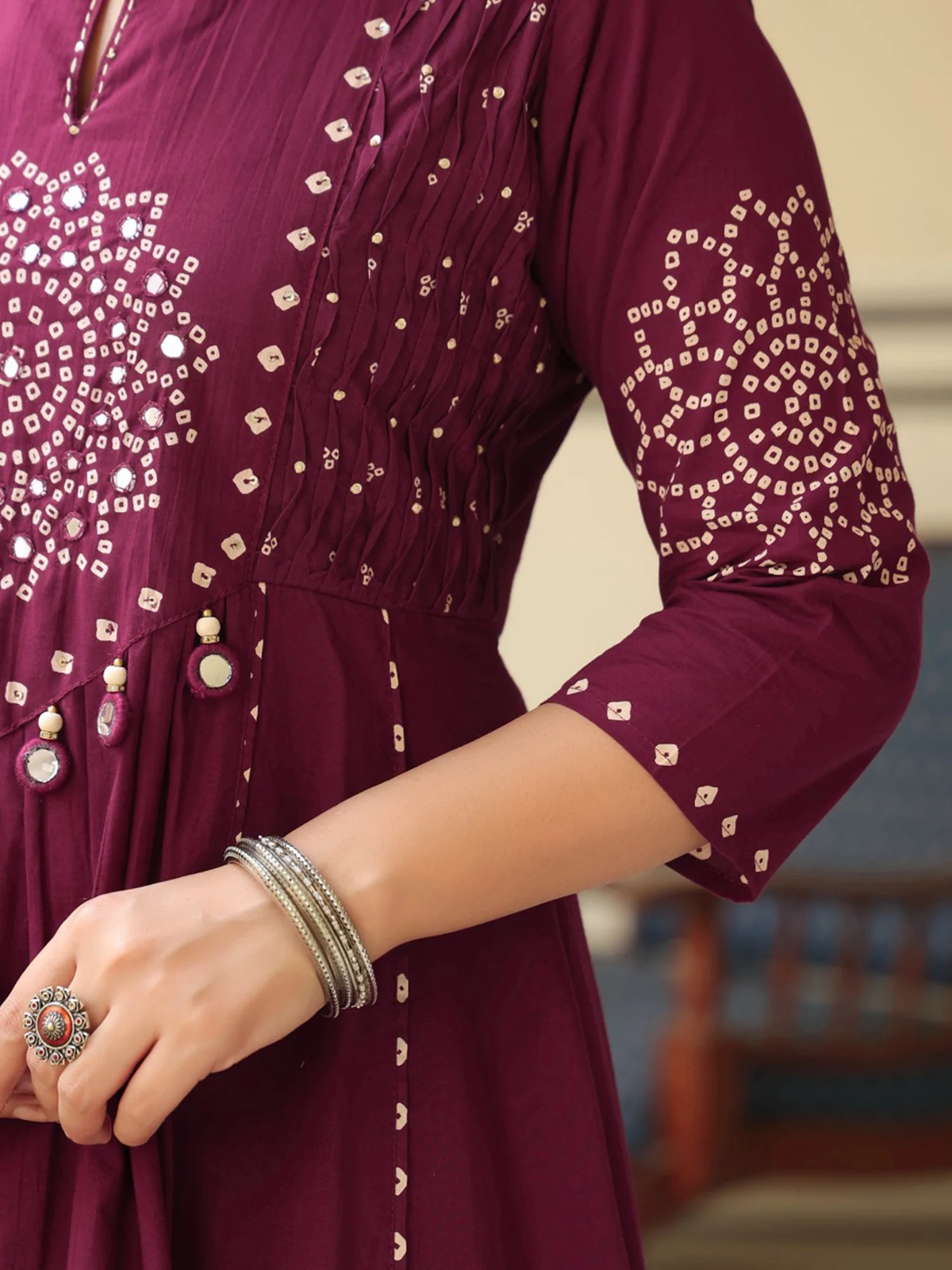 Close-up of a maroon dress with intricate gold patterns and jewelry.