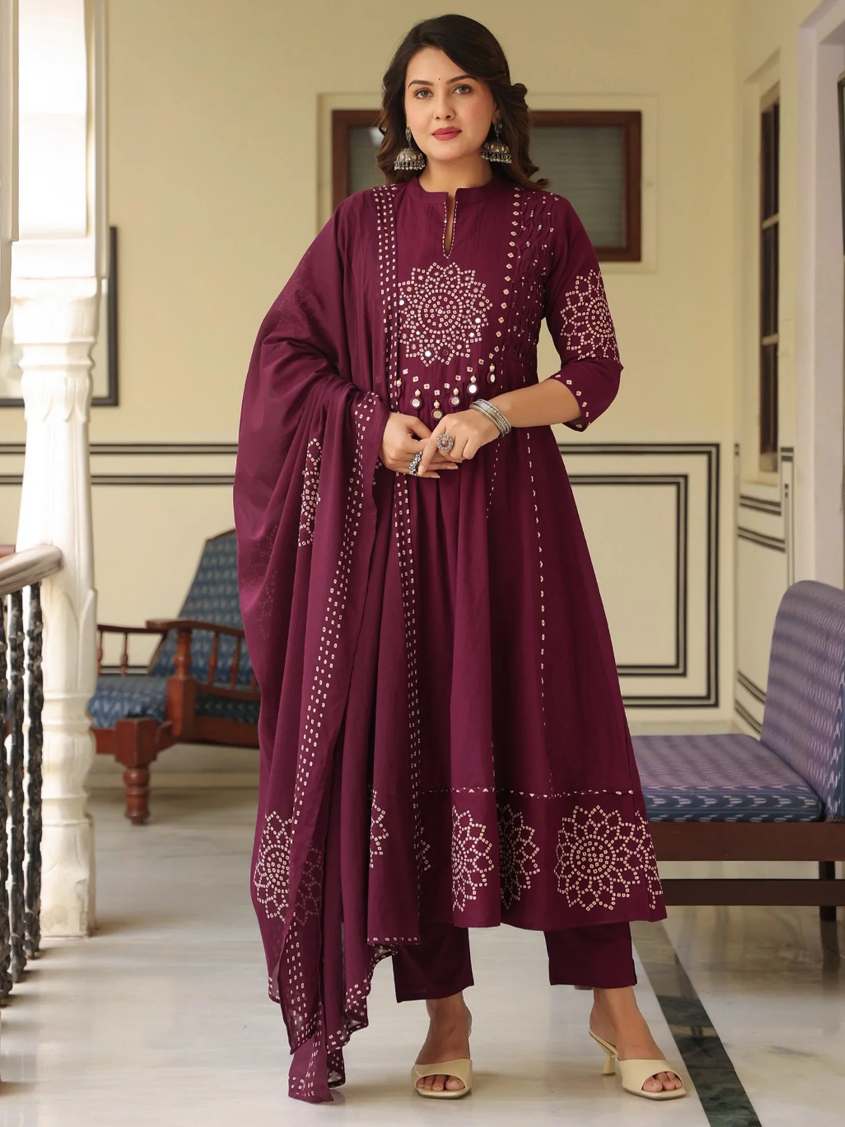Woman wearing a maroon traditional outfit with intricate patterns in an indoor setting.