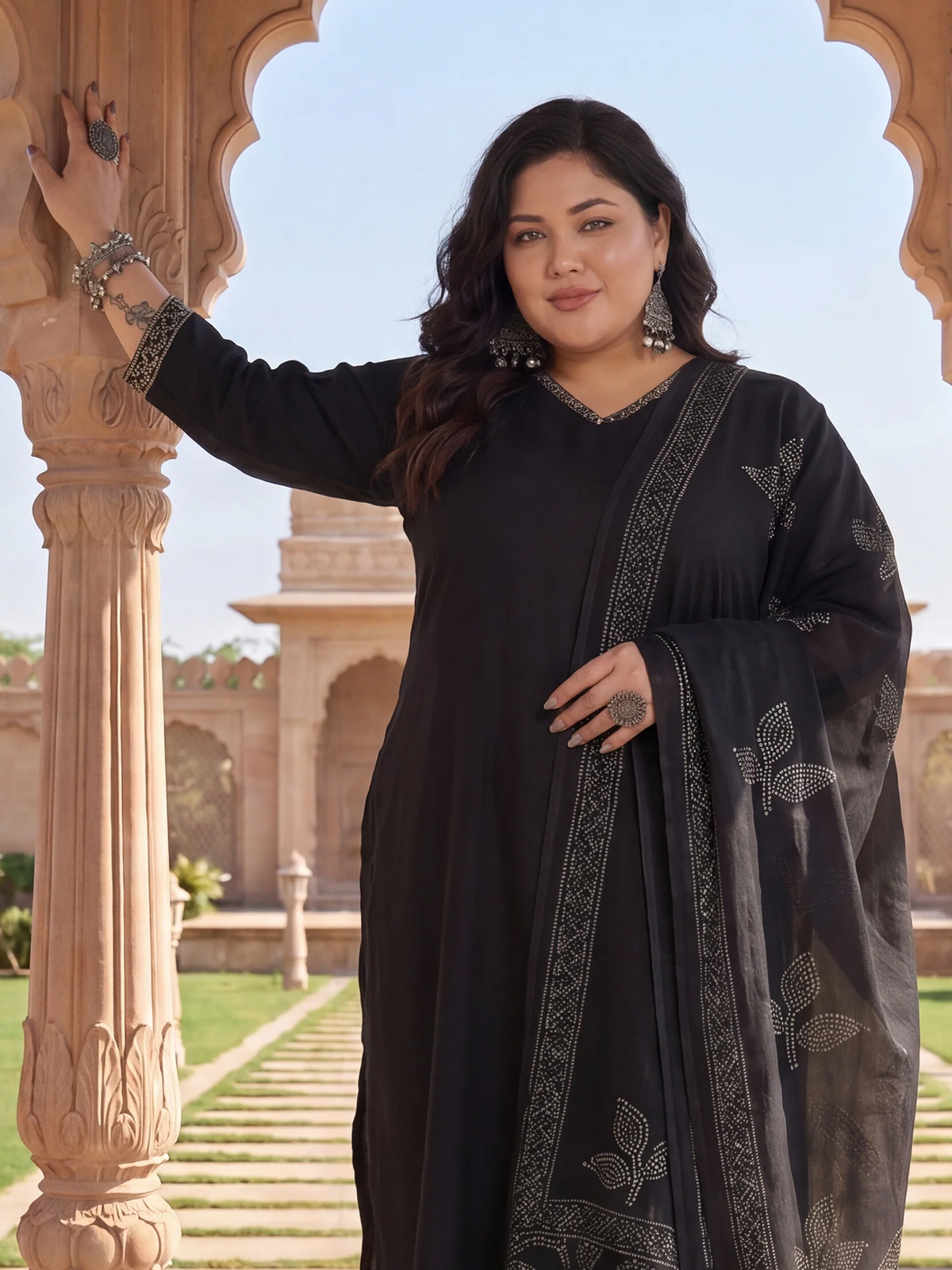 Woman in a black traditional outfit standing in an outdoor setting with architectural elements.