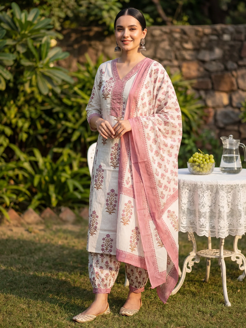 Woman in traditional outfit standing outdoors with a garden and table in the background