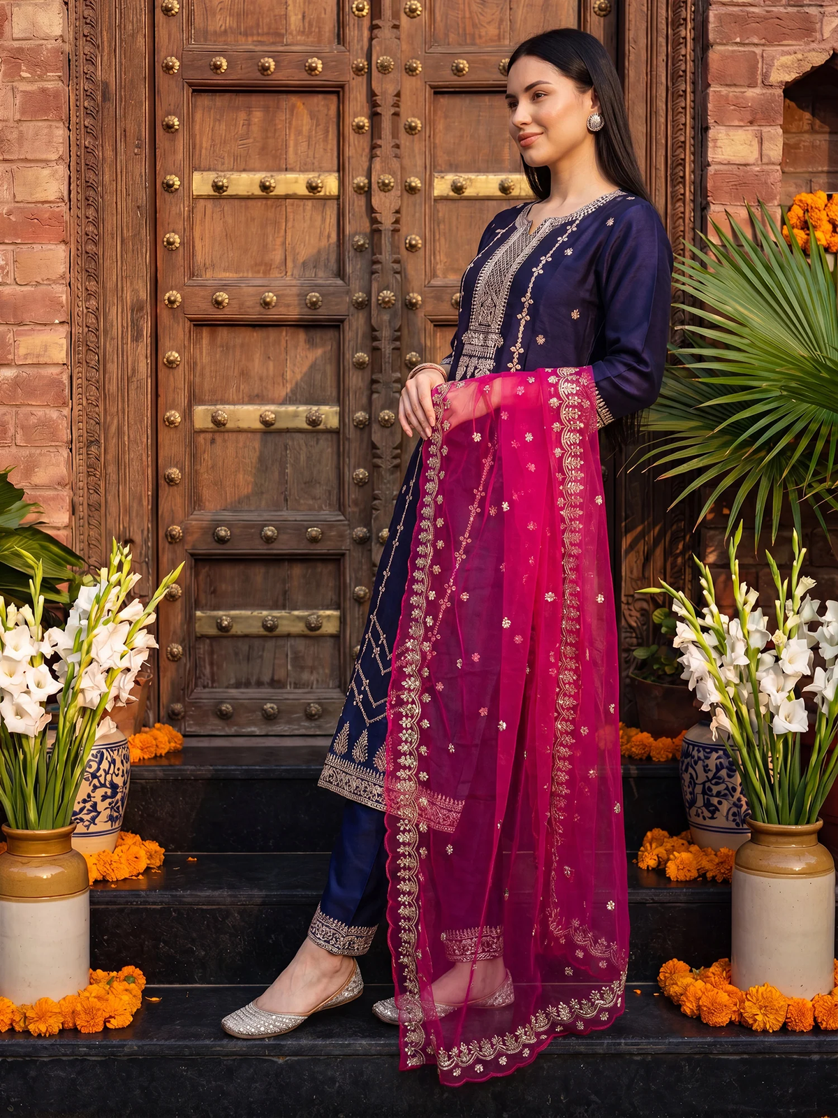 Woman in traditional outfit standing in front of a wooden door with floral decorations.