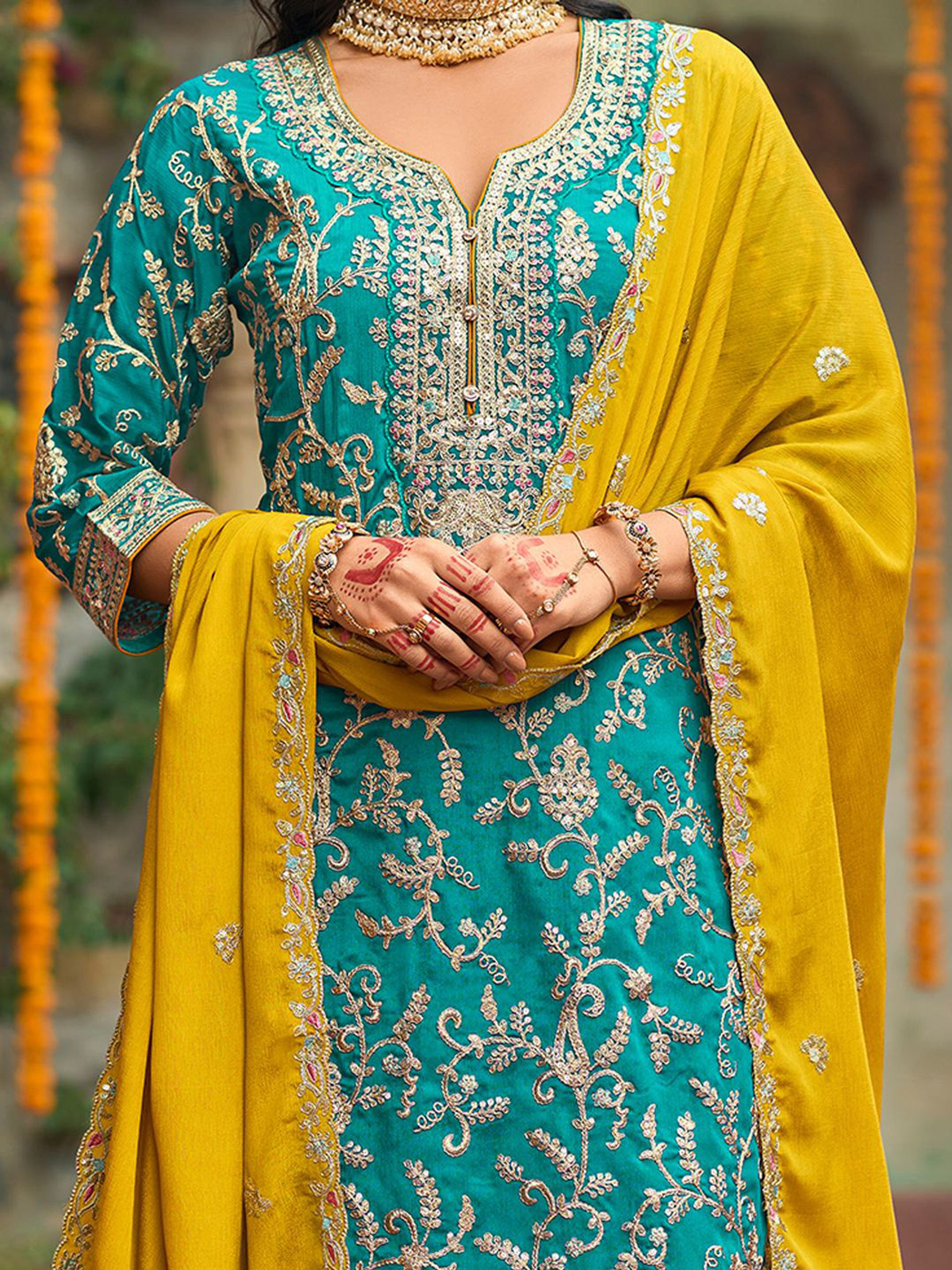 Woman wearing a traditional outfit with turquoise and yellow colors, featuring intricate embroidery.