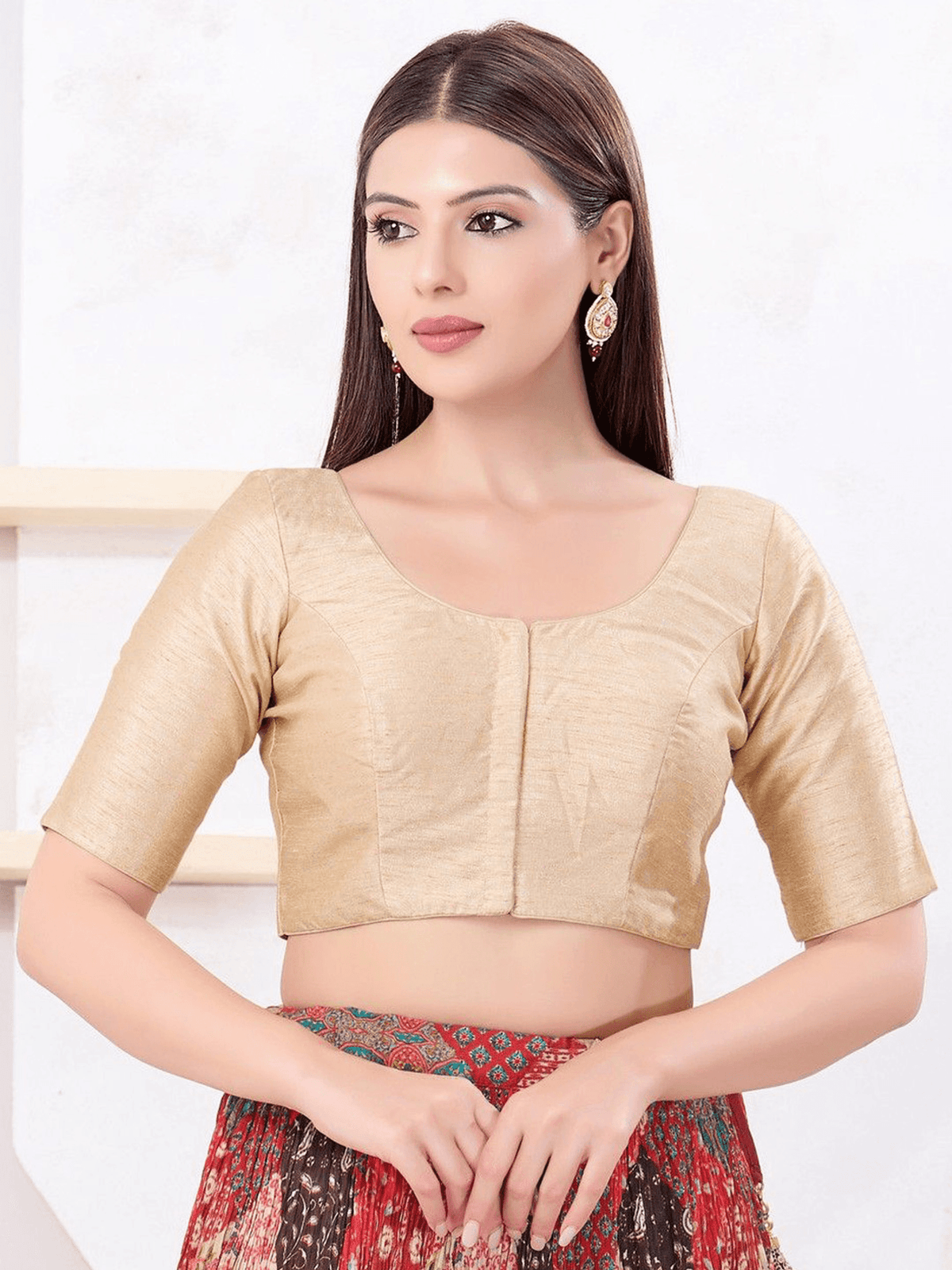 A woman modeling a beige short-sleeve crop blouse with a square neckline and front button detail, paired with a red patterned skirt.