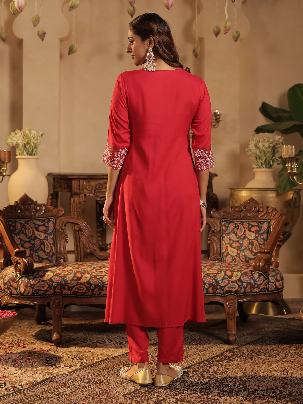 Woman in a red outfit standing in an ornate room with patterned furniture.