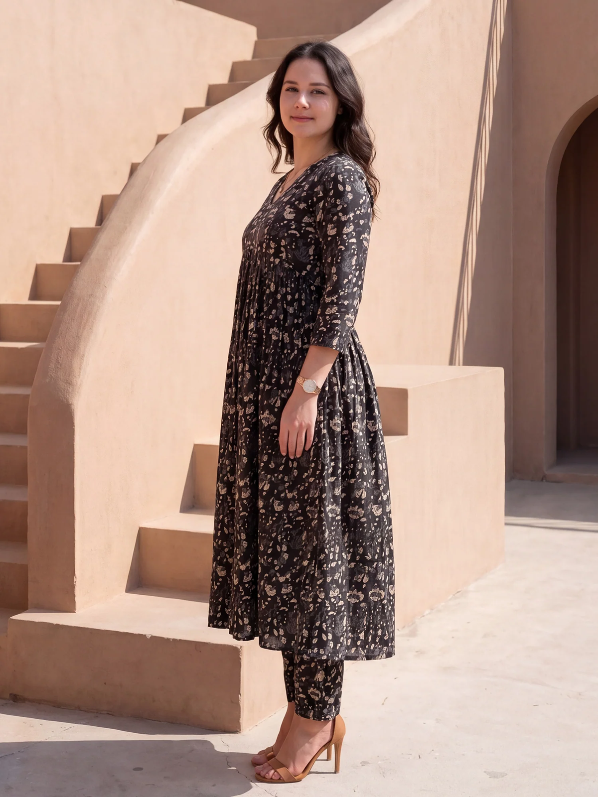 Woman in a black floral dress standing on stone steps with a beige wall in the background