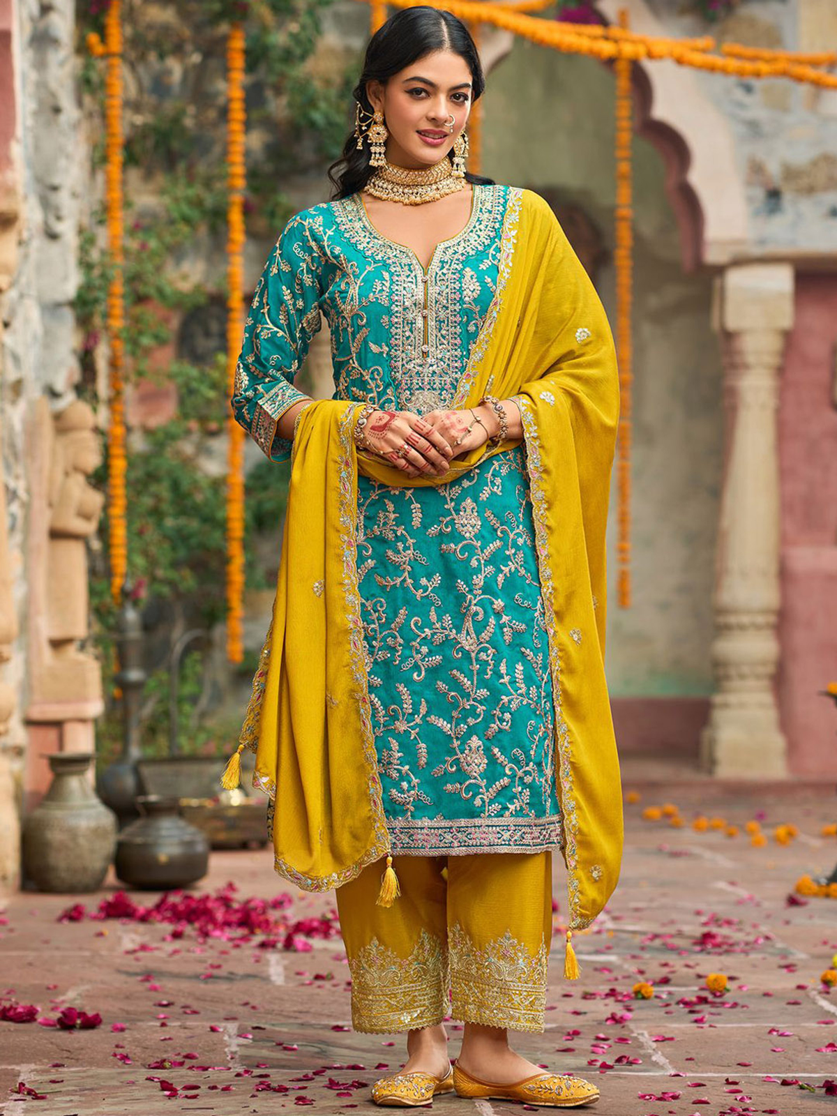 Woman in a traditional outfit with teal and yellow colors standing in an outdoor setting.