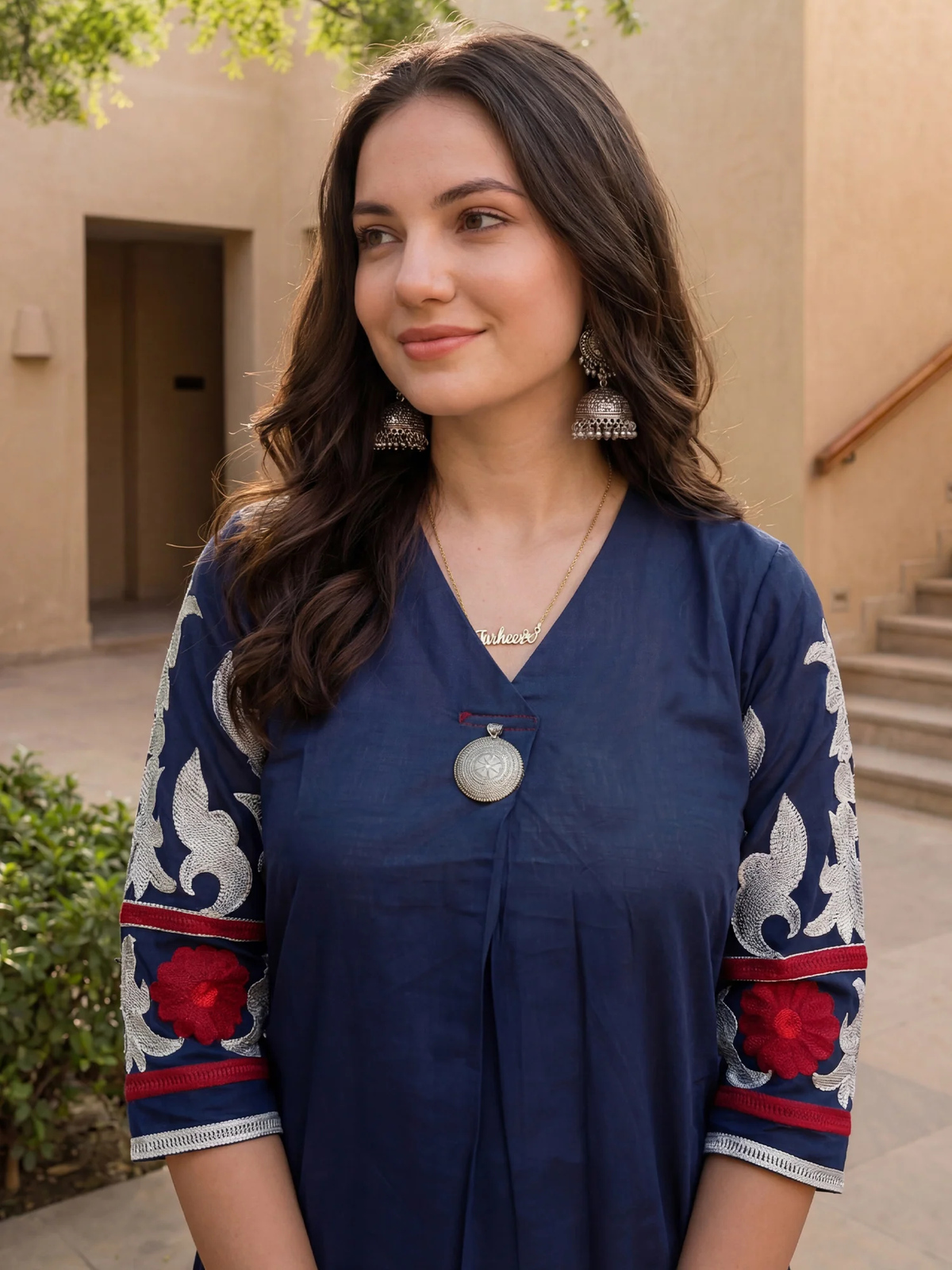 Woman wearing a blue traditional outfit with red and white patterns outdoors.