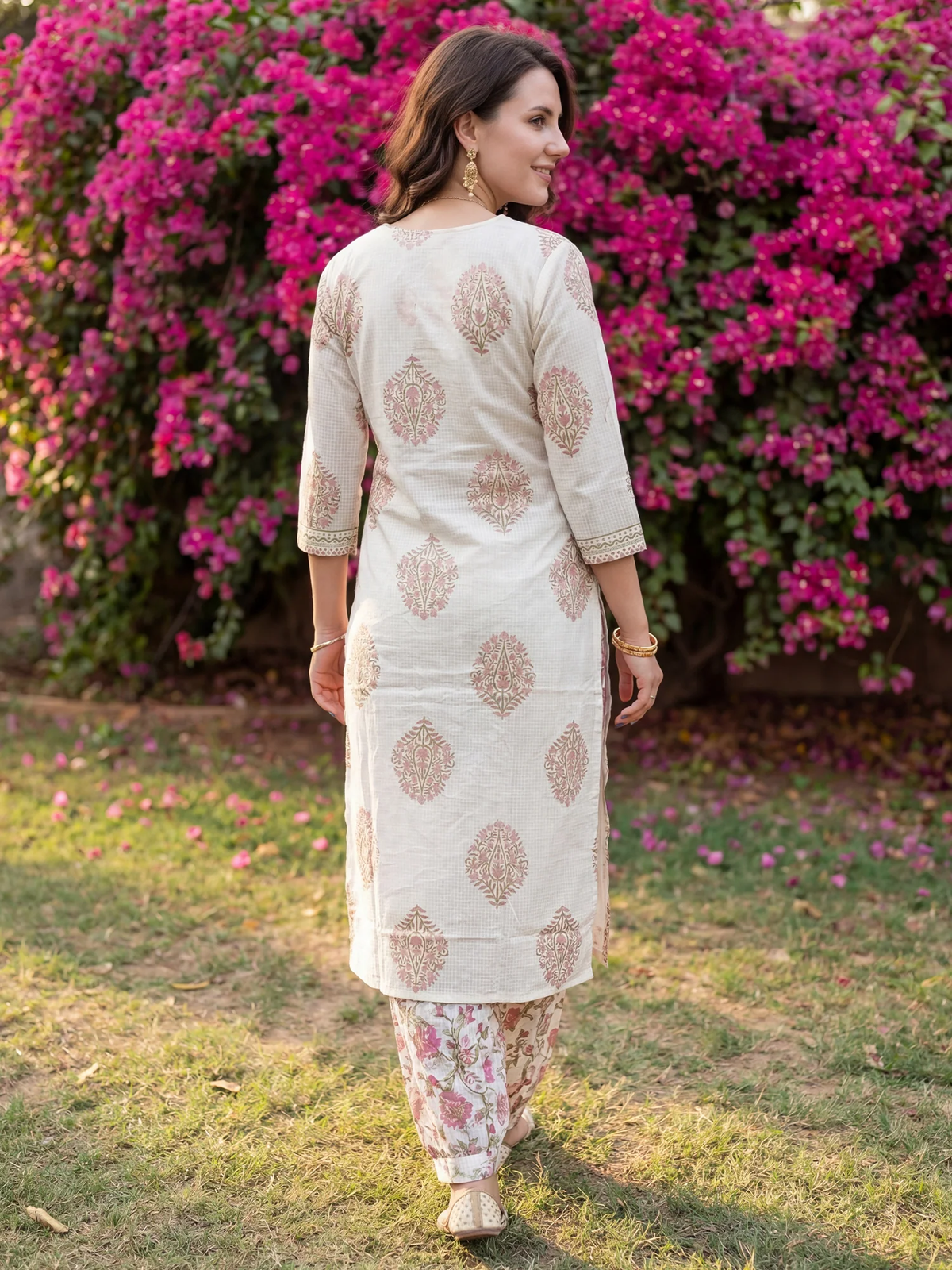 Woman in a traditional outfit standing in front of pink flowering bushes.