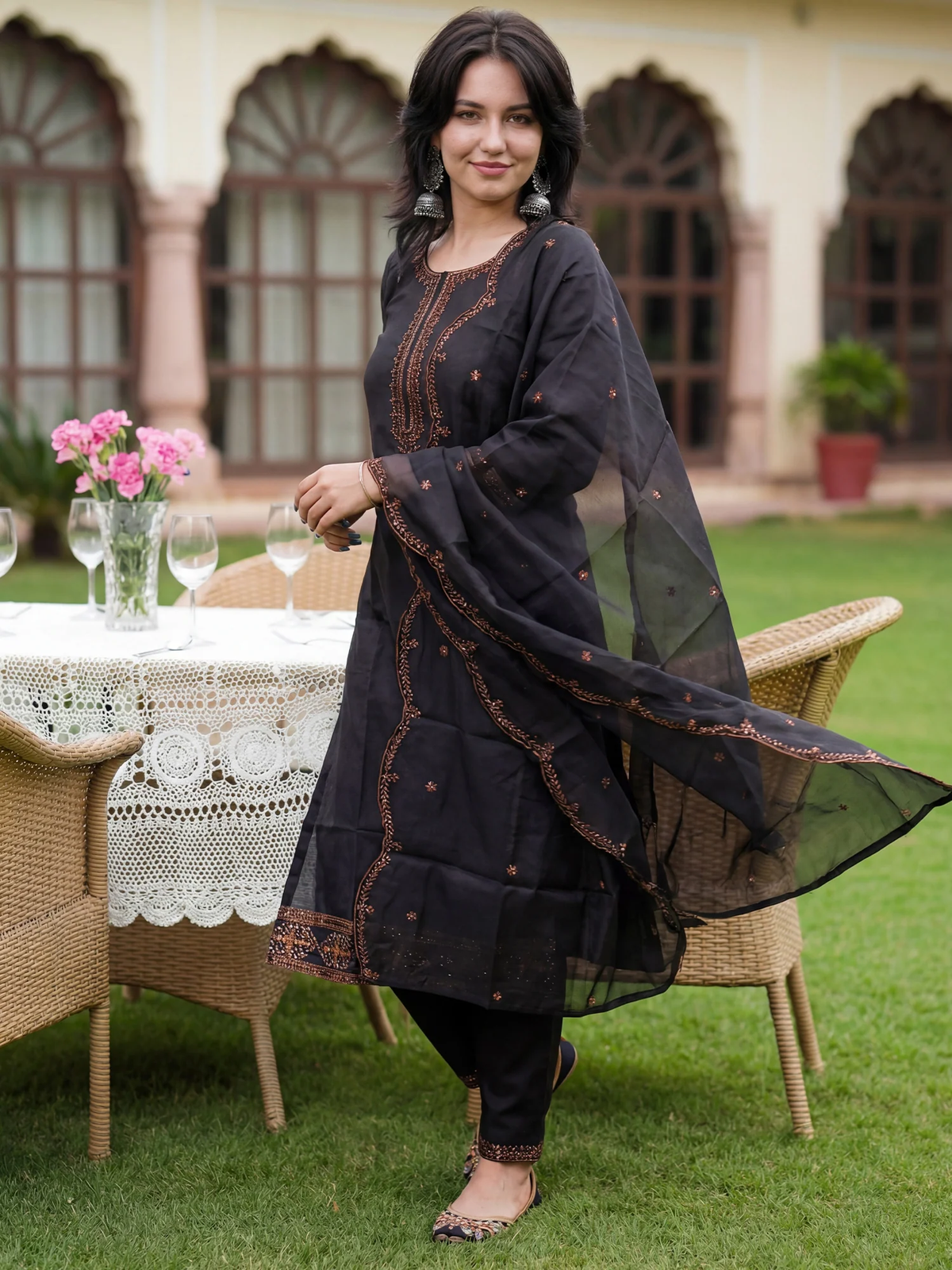 Woman in a black traditional outfit standing outdoors with a table and flowers in the background