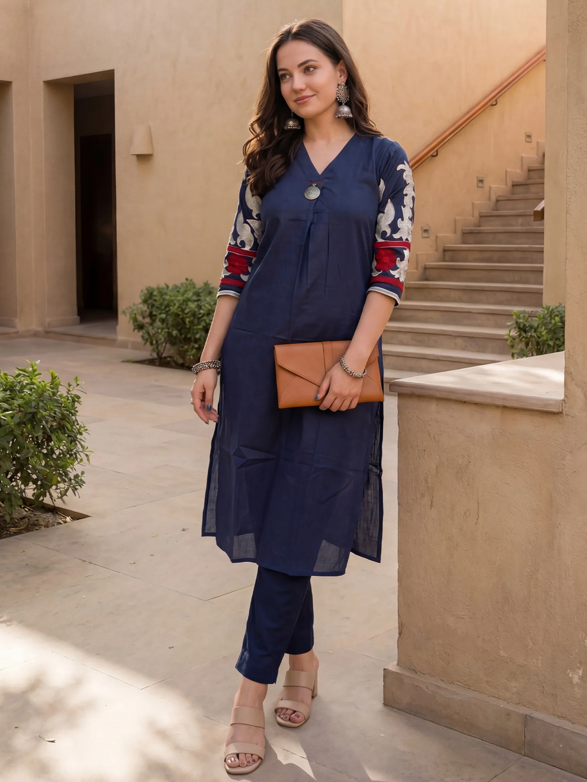 Woman in a navy blue outfit with a patterned top, holding a brown clutch, standing outdoors.