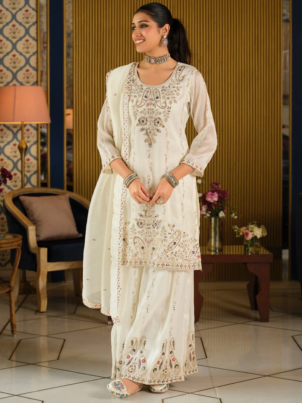Woman wearing a cream embroidered traditional outfit in an indoor setting.